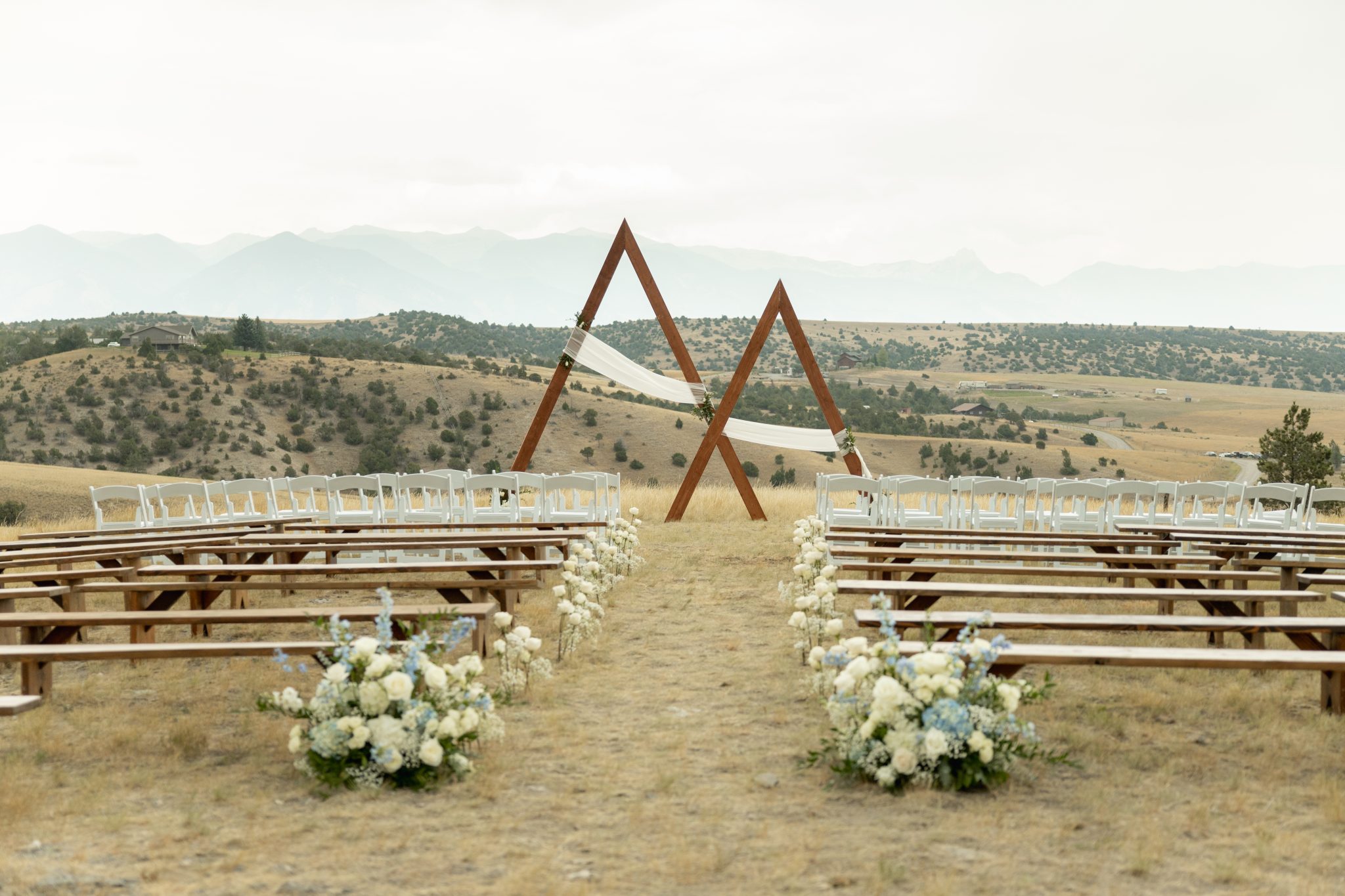 Outdoor Montana tented wedding ceremony featuring a modern wooden triangle arch with serene mountain views in the background.