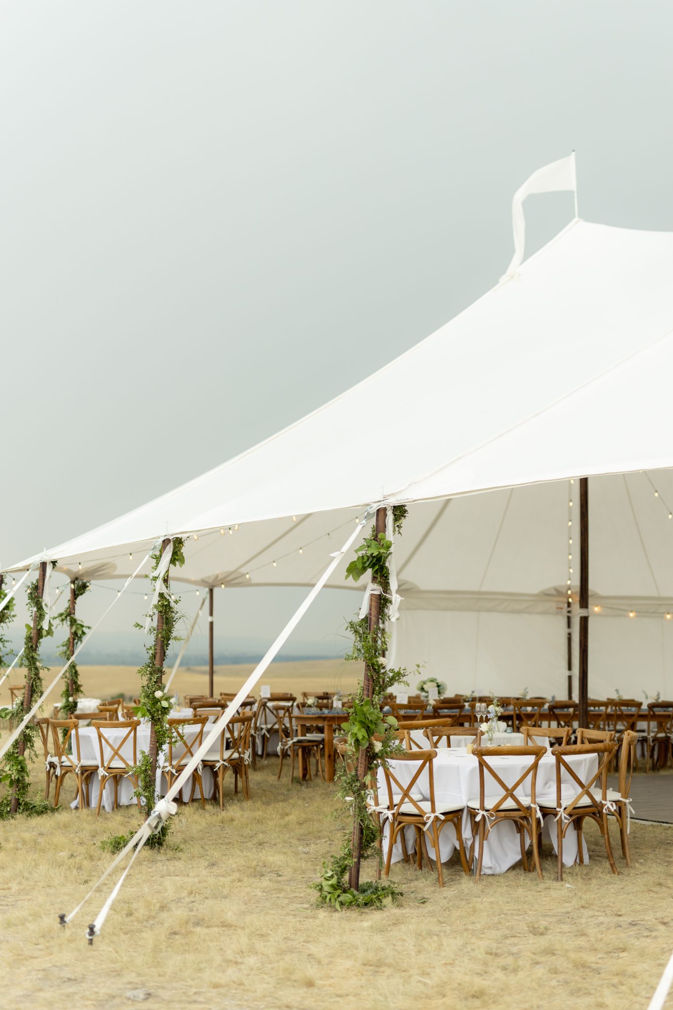 Elegant white wedding tent setup in Montana with rustic wooden chairs and greenery décor, perfect for a summer wedding reception in the countryside.