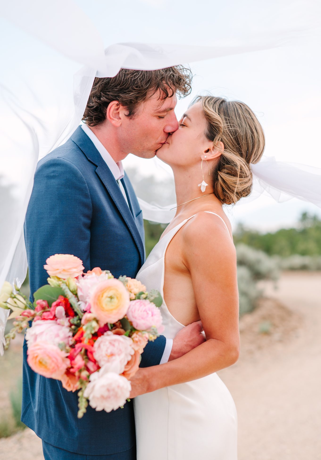 Bride and groom share a kiss under a flowing veil at a scenic Taos wedding.