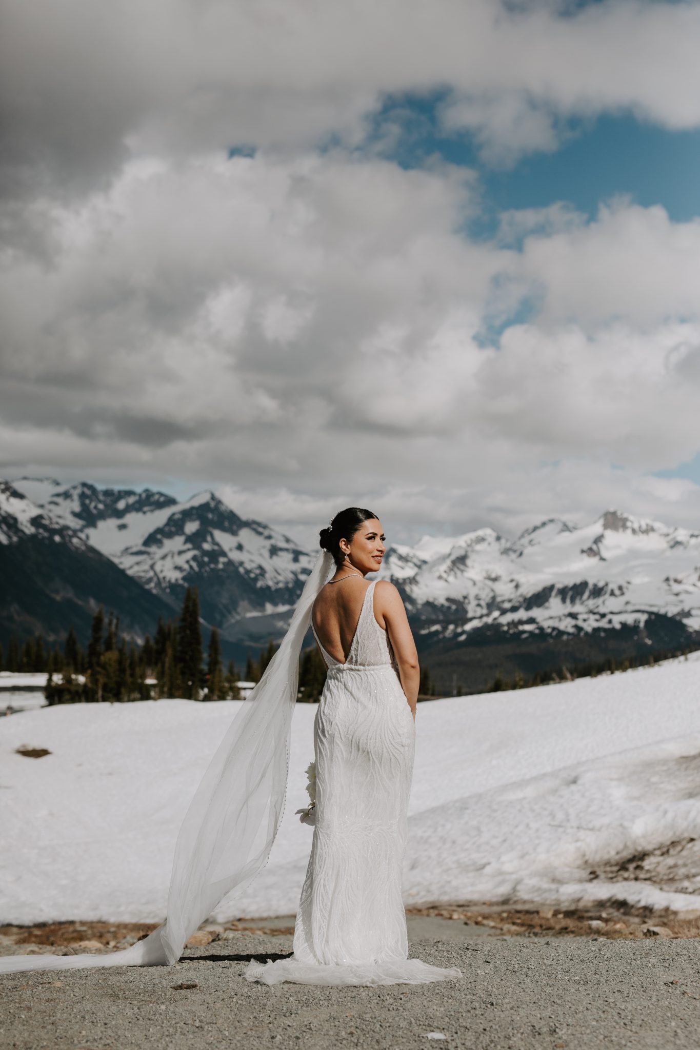 The bride in an elegant gown, standing amidst the stunning mountain scenery of Whistler on her wedding day.