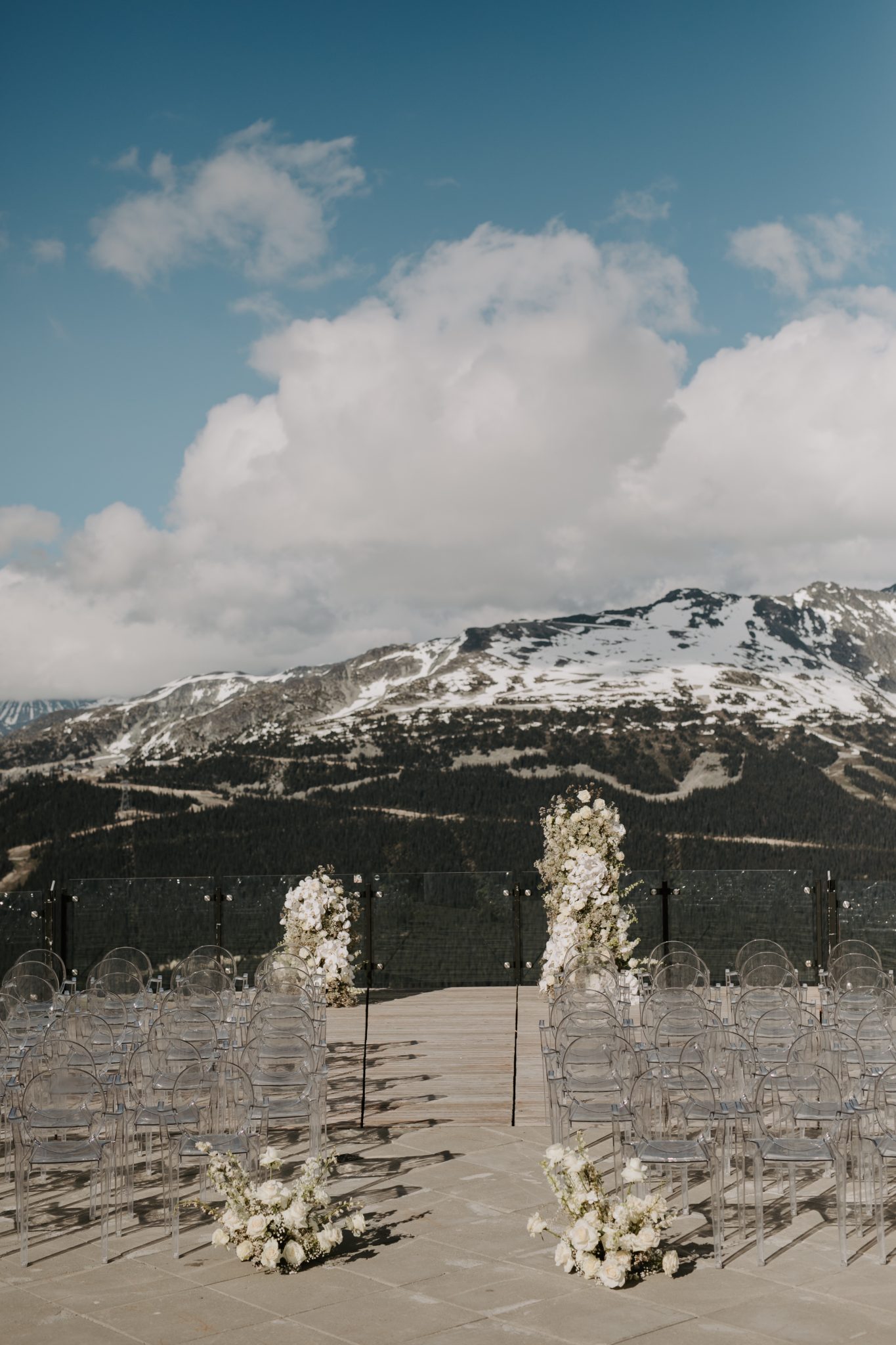 Stunning mountain-view wedding ceremony setup in Whistler, featuring clear chairs and floral arrangements with snow-capped peaks in the background.