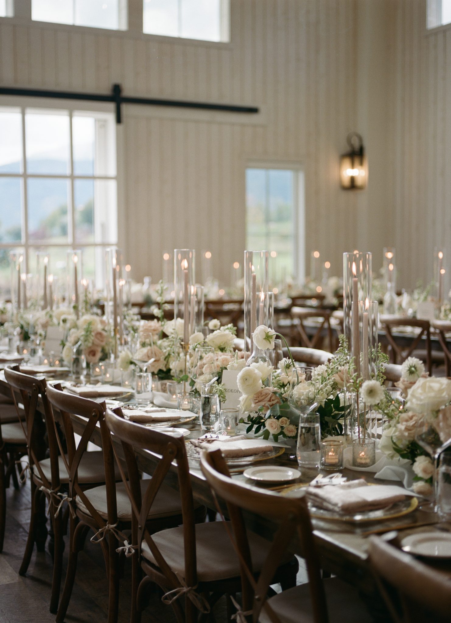 Long reception tables beautifully arranged with white and blush floral centerpieces, tall candles, and natural wood chairs, enhancing the romantic ambiance of the Utah summer wedding.