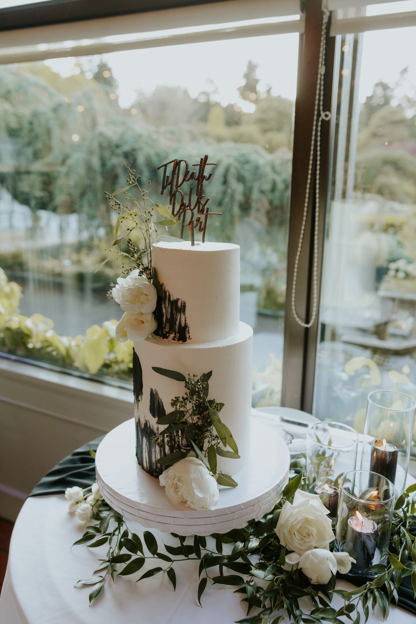 Minimalist white three-tiered wedding cake decorated with greenery and black candles for a Black and White Vancouver Wedding.