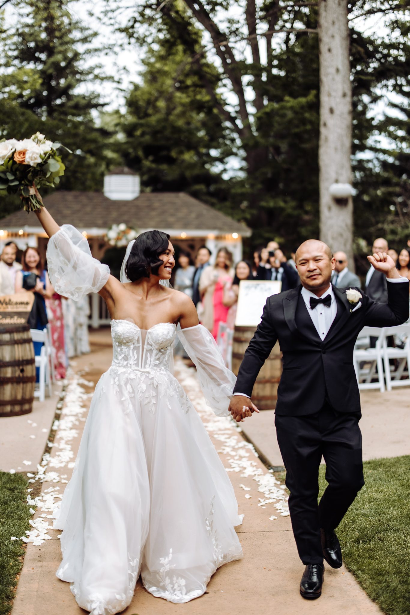 A joyful couple just married at the Tapestry House in Colorado, celebrating in front of a charming gazebo surrounded by lush greenery.