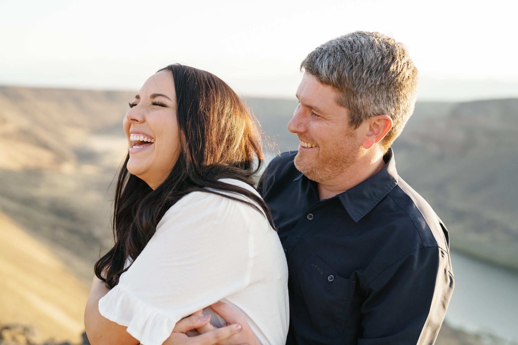 Couple laughing together with a scenic Idaho landscape in the background during their engagement session