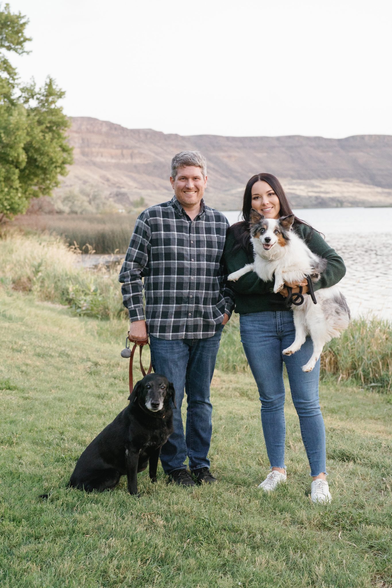Engaged couple posing with their dogs by a lakeside during their Idaho engagement session