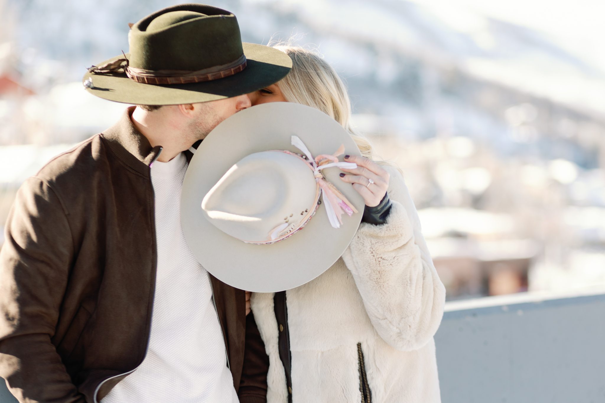 Romantic moment as the couple shares a kiss behind their stylish hats during a scenic Park City engagement session.
