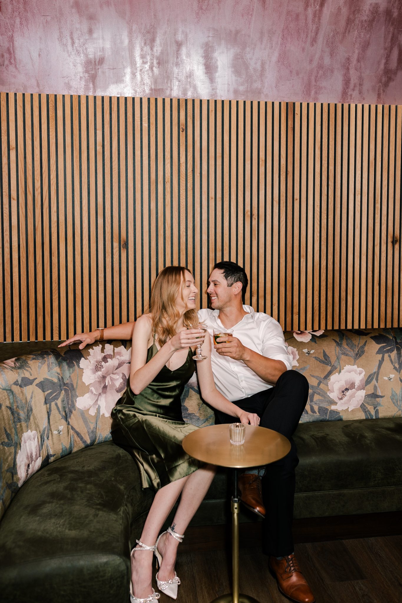 A playful couple enjoying drinks on a floral-patterned sofa in a trendy Boise venue, capturing the charm of city engagements in Boise.