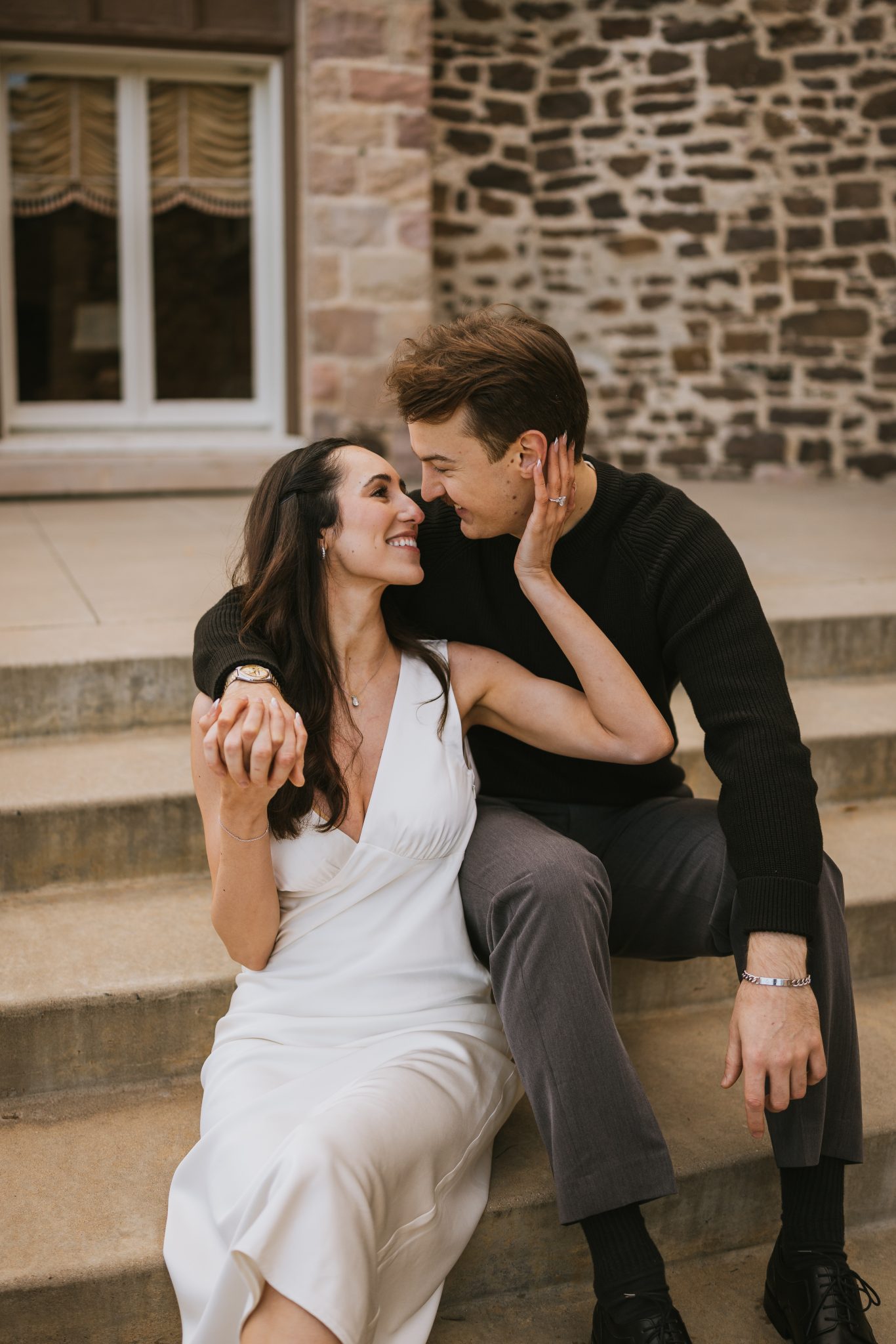 A candid moment of the couple sharing a smile while sitting on the steps of Highlands Ranch Mansion during their fall engagement session.