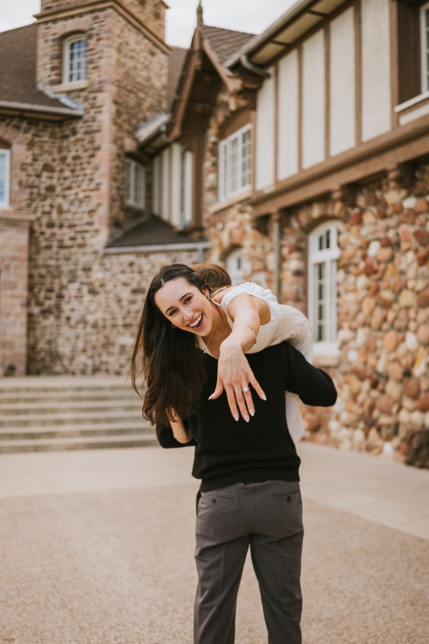 The groom-to-be lifts his fiancée in front of the stone facade of Highlands Ranch Mansion during their fall engagement session.
