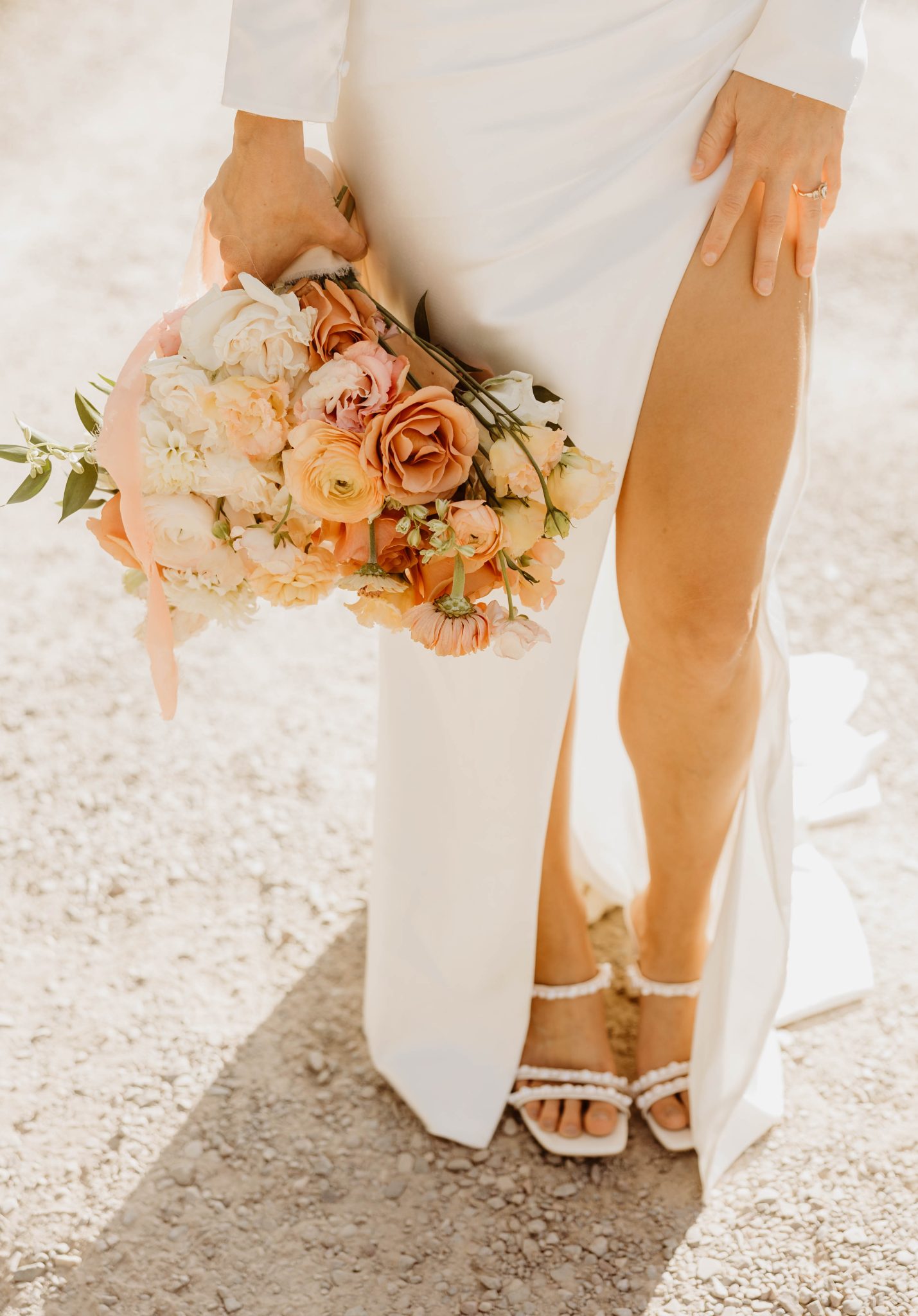 A detailed shot of the bride holding a bouquet of soft orange and blush-toned flowers against her white gown, emphasizing the soft orange wedding color palette.