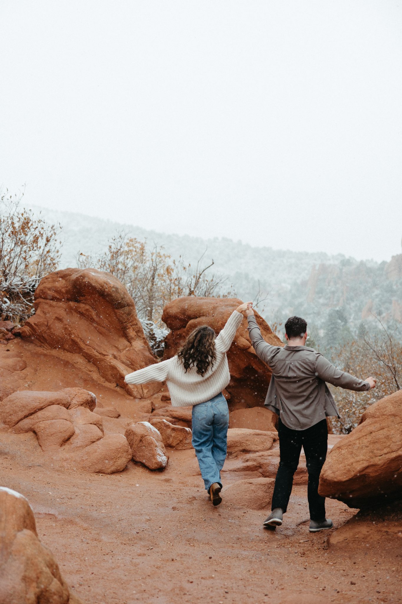 The couple holds hands and dances along the scenic trails, featuring iconic red rock landscapes during their Colorado fall engagements.