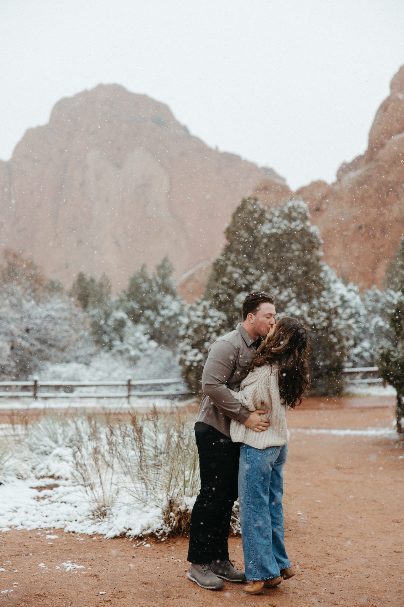 A couple shares a sweet kiss surrounded by fresh snow and stunning red rock formations in Colorado fall engagements.