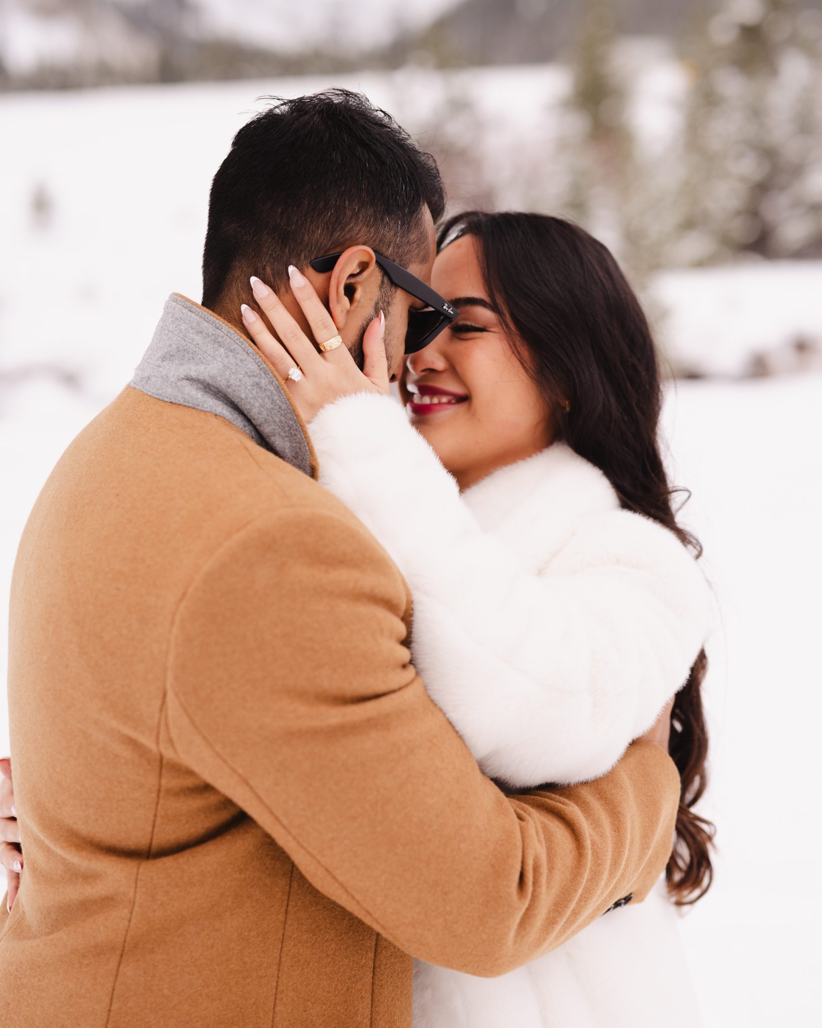 A joyful couple embraces in the snow after a heartfelt Colorado surprise proposal, with the bride-to-be showing off her engagement ring.