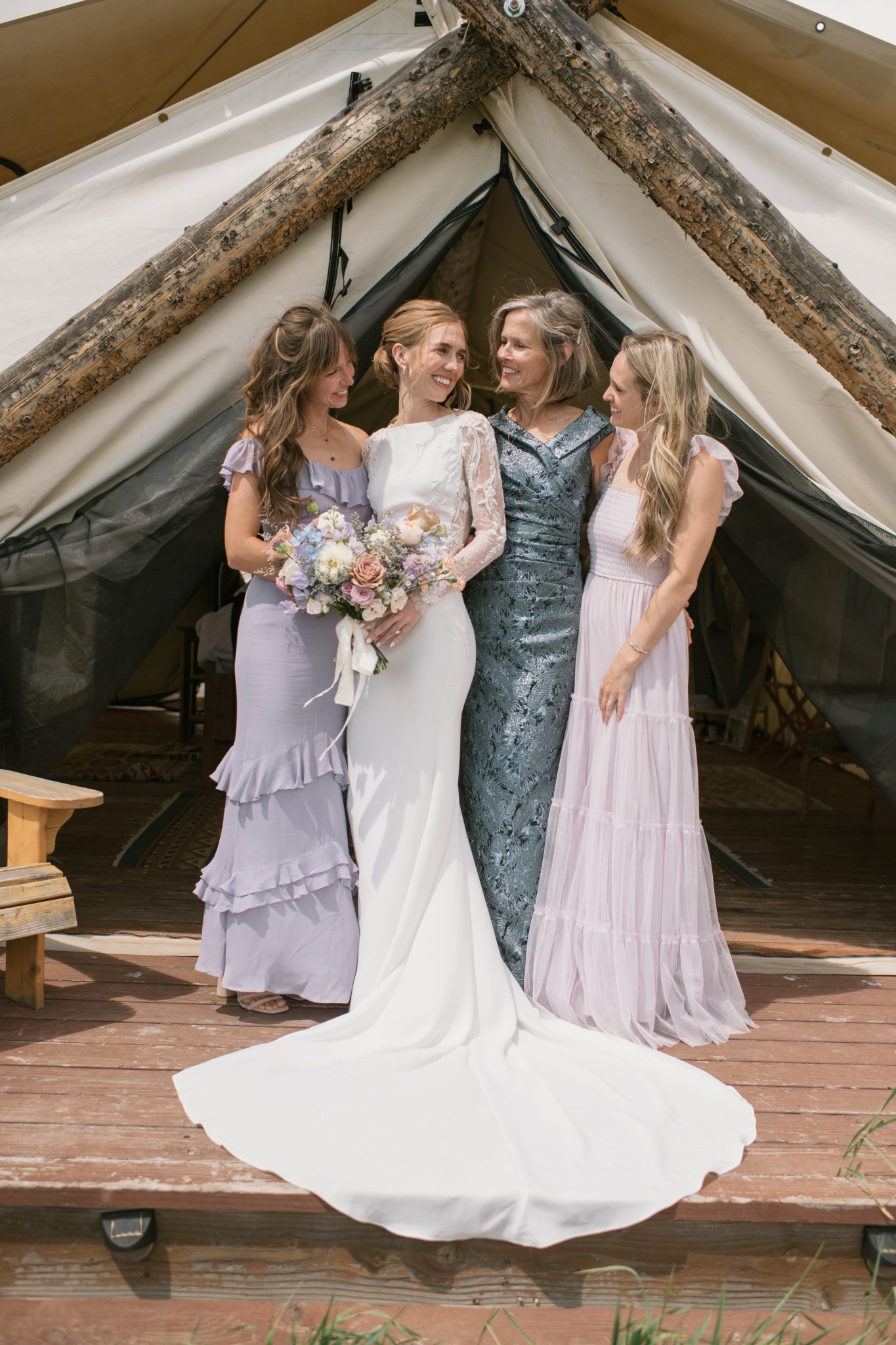 A bride poses with her bridesmaids and mother in soft pastel dresses outside a glamping tent at a Four Seasons Resort Vail wedding.