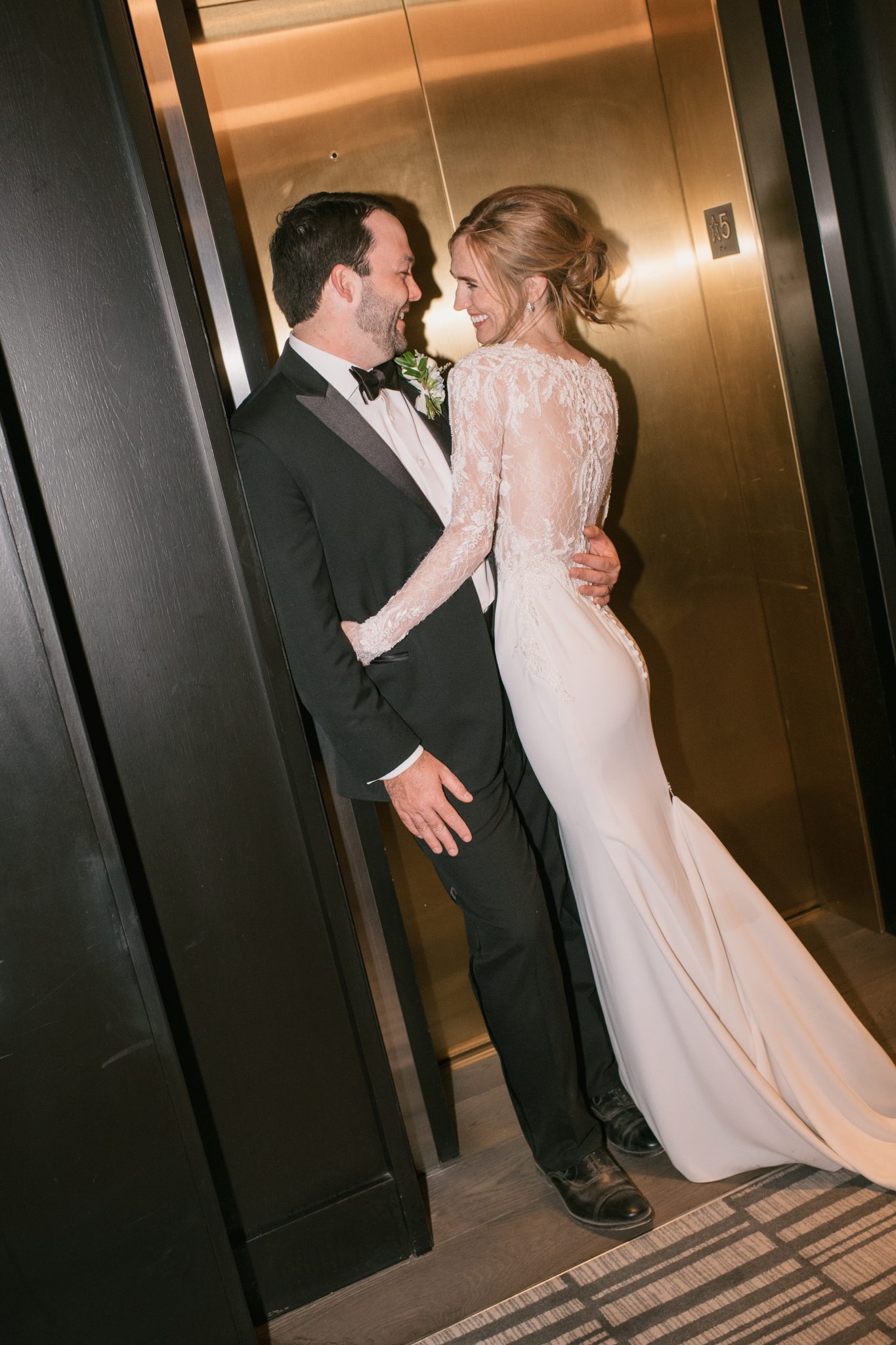 A bride and groom share an intimate moment near a luxurious elevator at a Four Seasons Resort Vail wedding, with elegant attire and a golden backdrop.