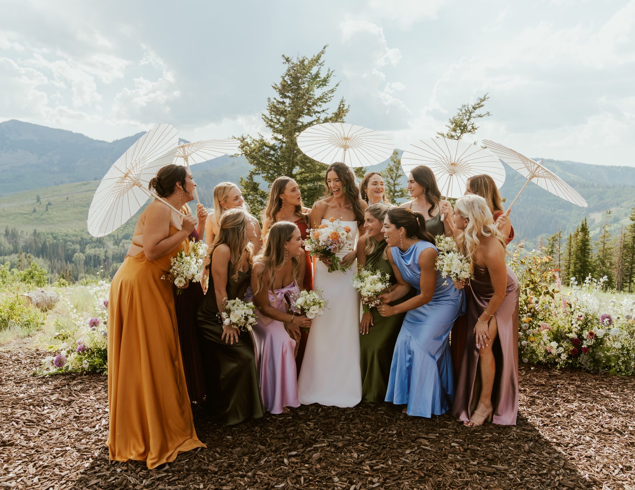 A joyful bridal party posing with pastel parasols against a scenic mountain view at a Garden inspired Utah wedding.