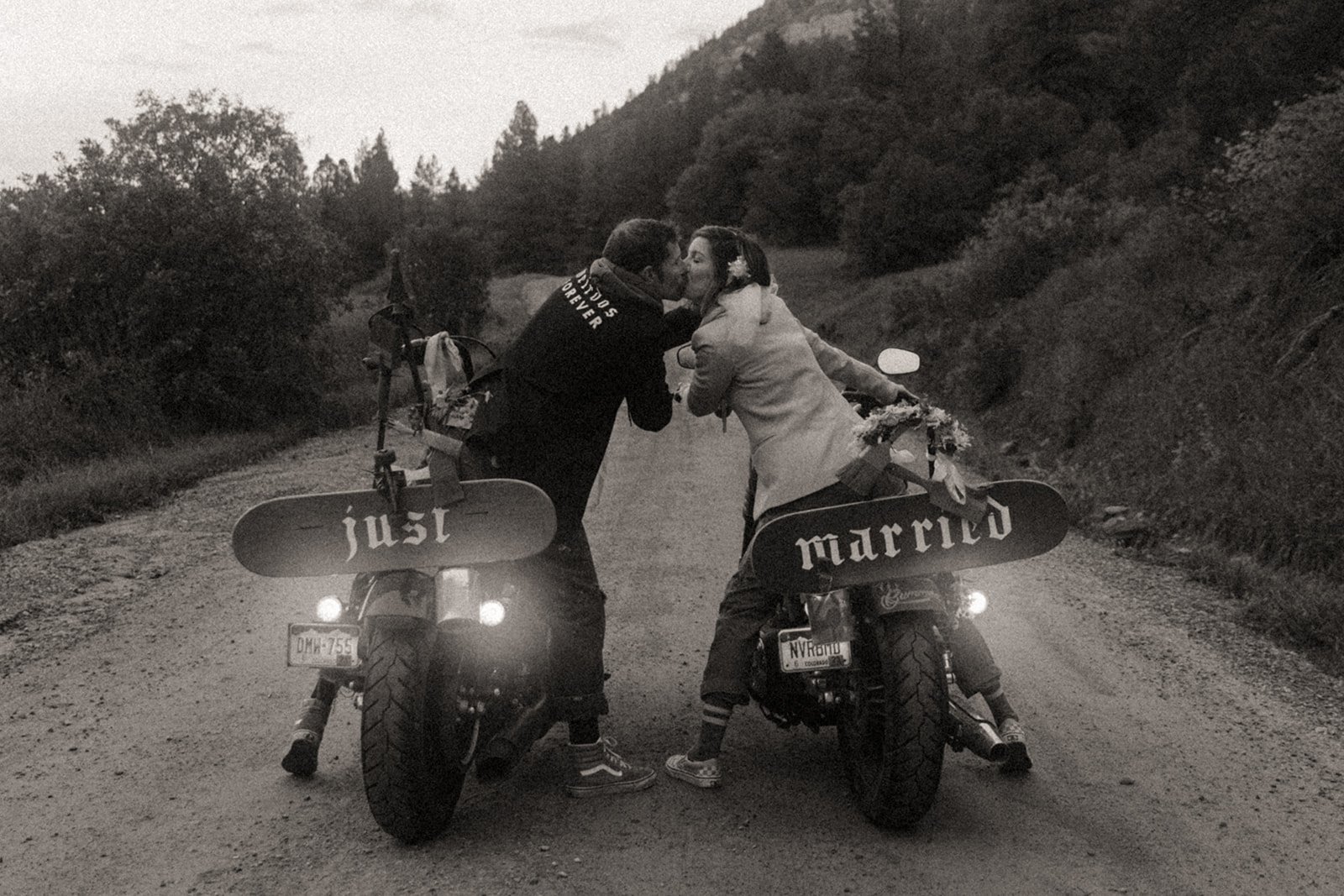 A black-and-white romantic kiss shared between the couple riding motorcycles with "Just Married" signs during their Hanna Irene Motion Pictures Durango Elopement.