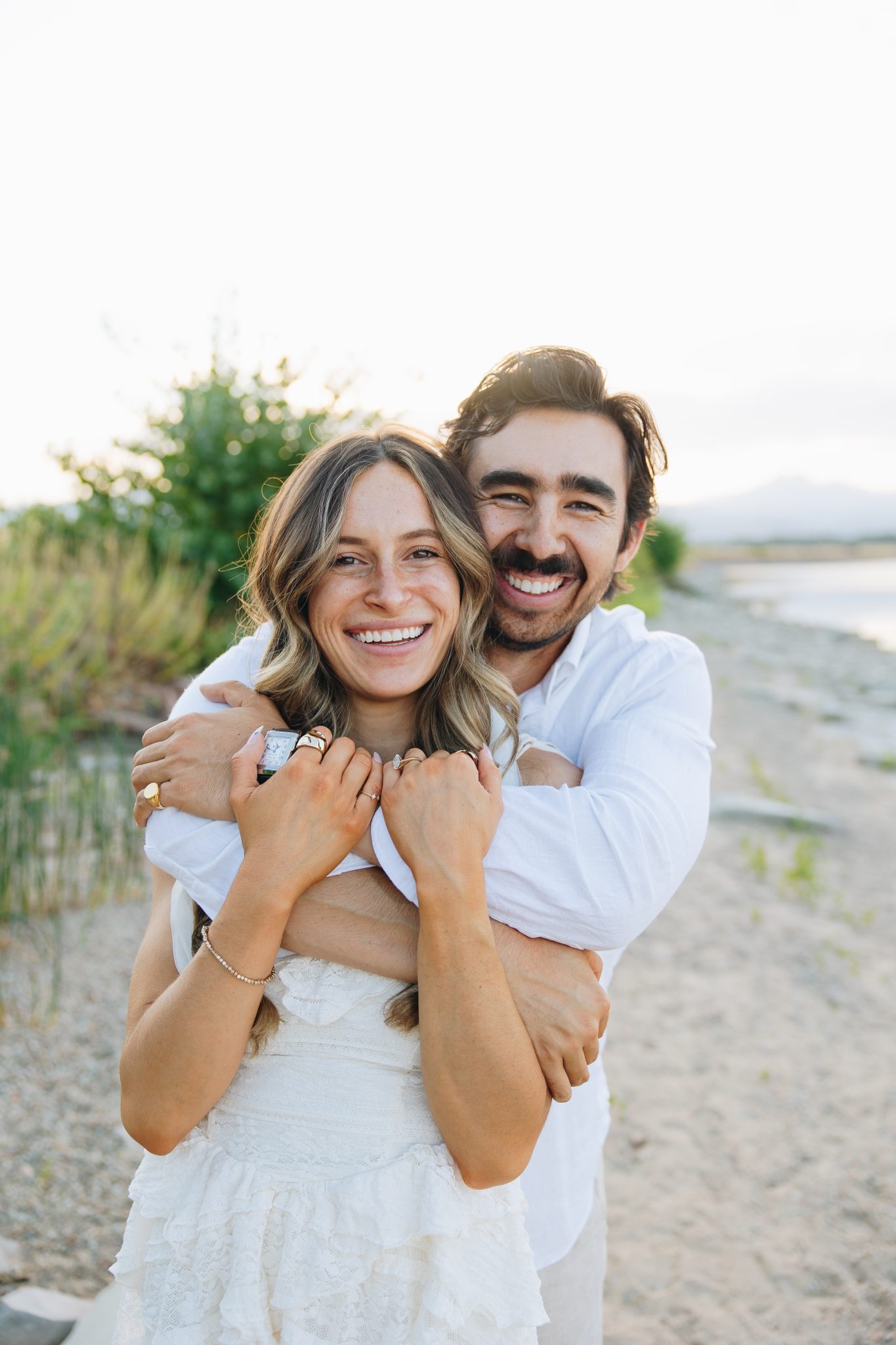 The couple embraces with big smiles on a scenic lakeside path, capturing the warmth of their fall Loveland engagements.
