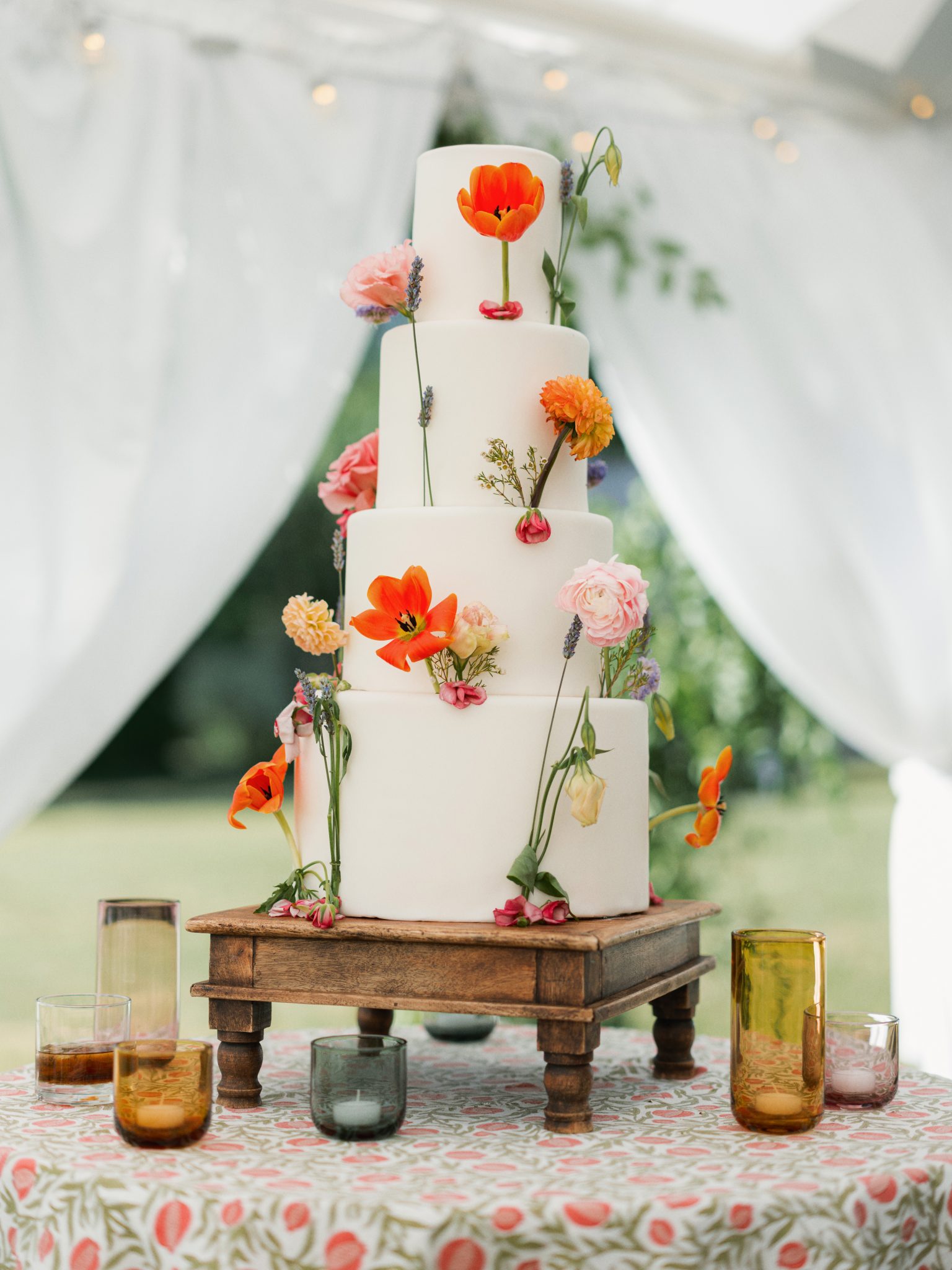 A minimalist white wedding cake adorned with fresh flowers, displayed on a wooden stand, adding a charming touch to a Montana farm wedding.