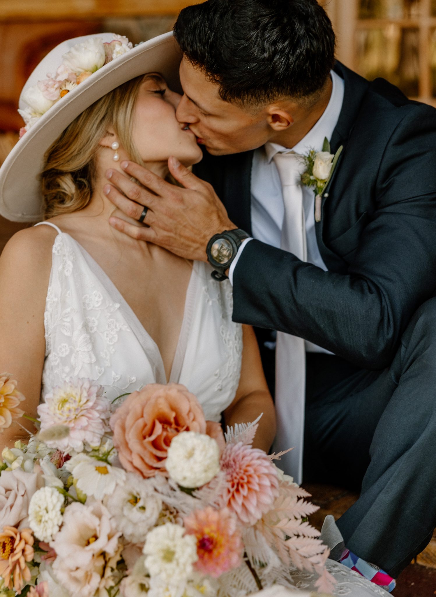 Bride and groom share a romantic kiss during their Western Durango summer wedding, surrounded by soft floral bouquets and bridal hat details.