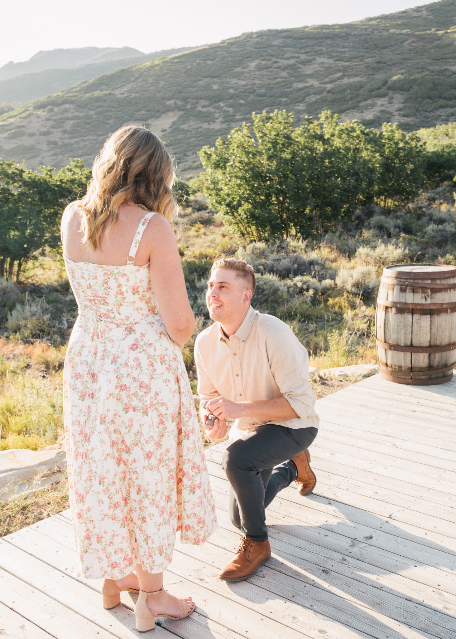A heartfelt Utah wedding proposal with the groom-to-be kneeling on a rustic wooden deck surrounded by scenic mountain views.