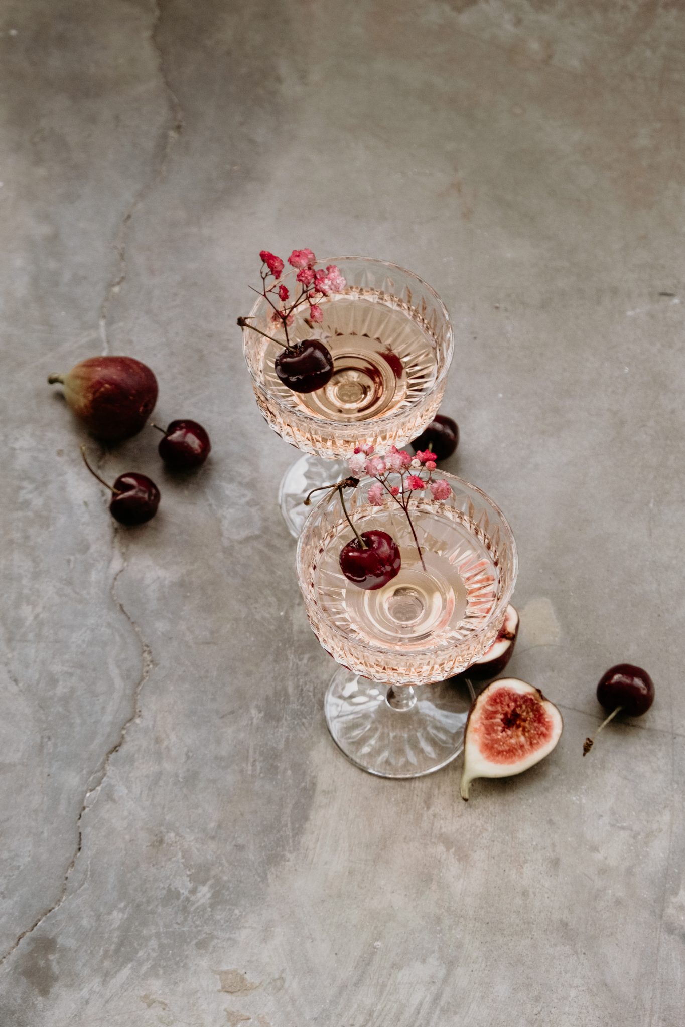 Crystal coupe glasses with pink champagne garnished with cherries and baby's breath, styled for a luxurious Valentine's Day Editorial.