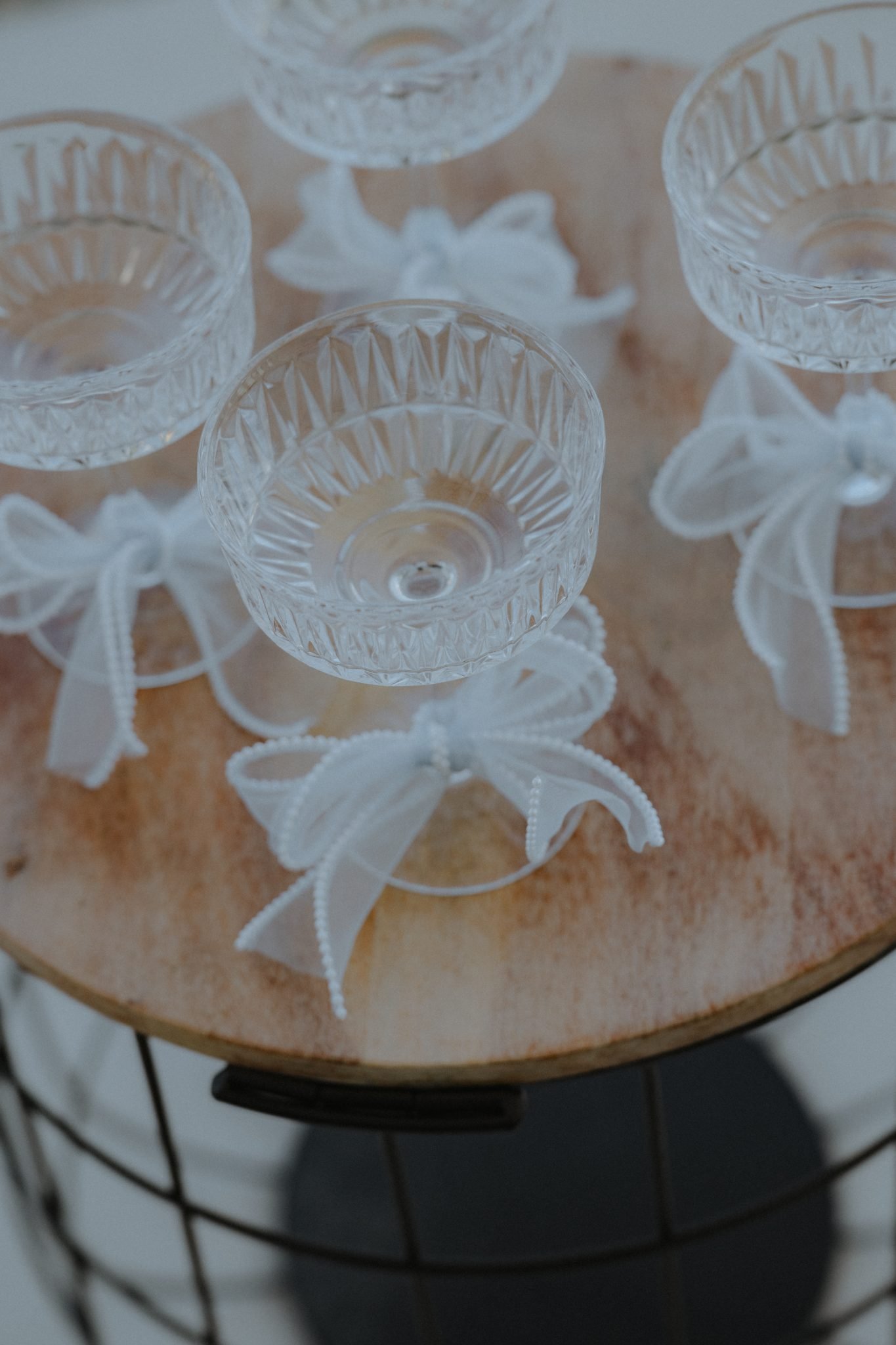 Crystal coupe glasses tied with white ribbons displayed on a rustic wooden tray, adding a refined touch to the white and blue wedding decor.