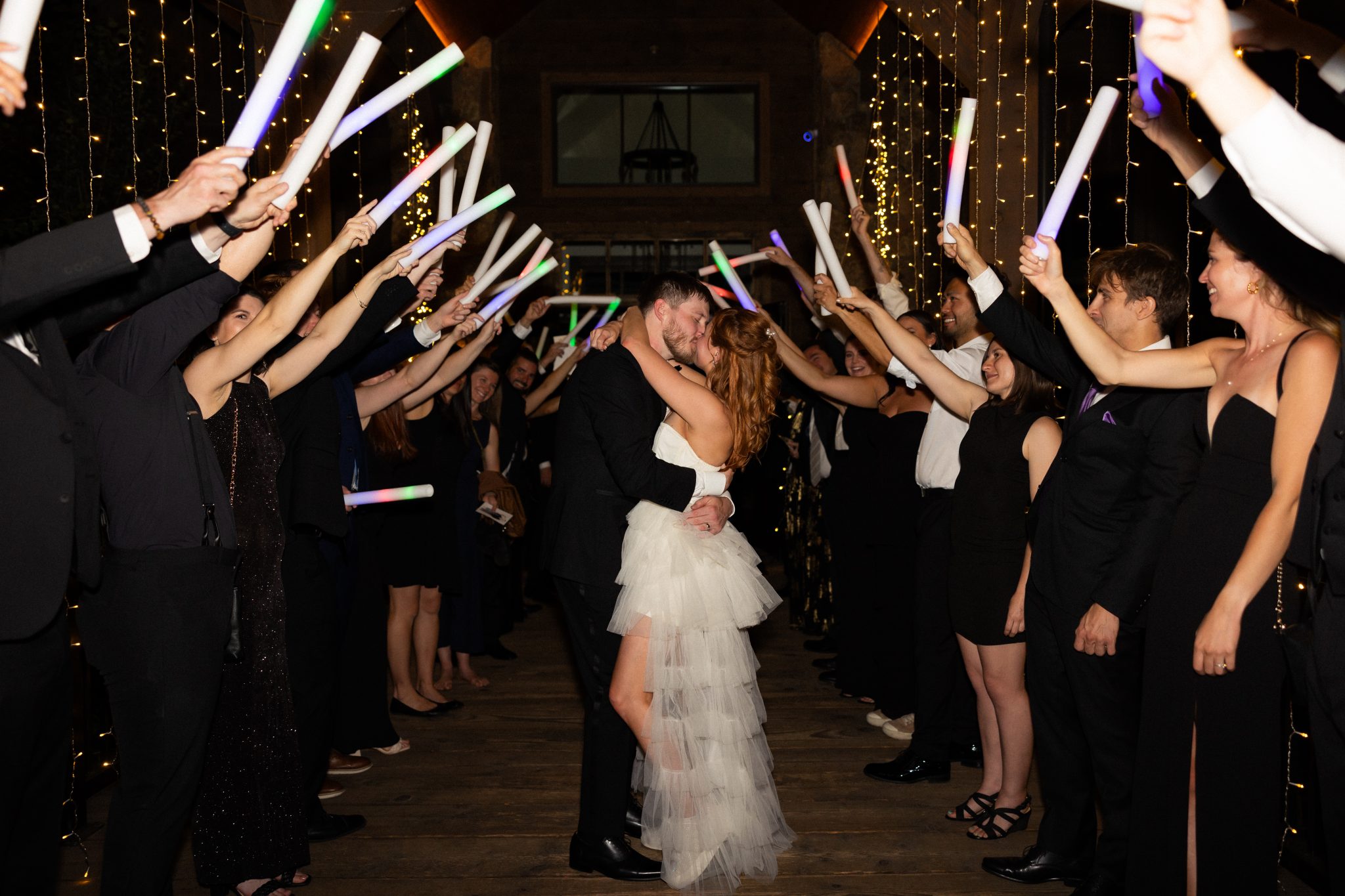 A magical grand exit featuring the couple kissing under a tunnel of guests holding glowing light sticks at an Estes Park wedding.