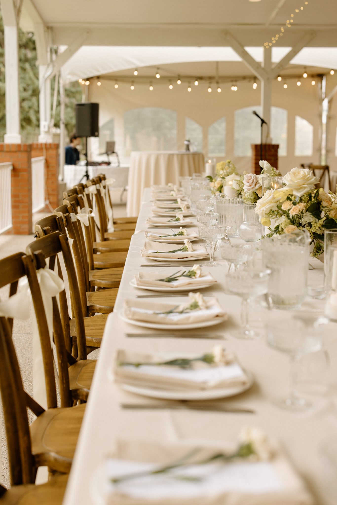 Long reception table with rustic wooden chairs and soft floral centerpieces at an Outdoor Alberta wedding.