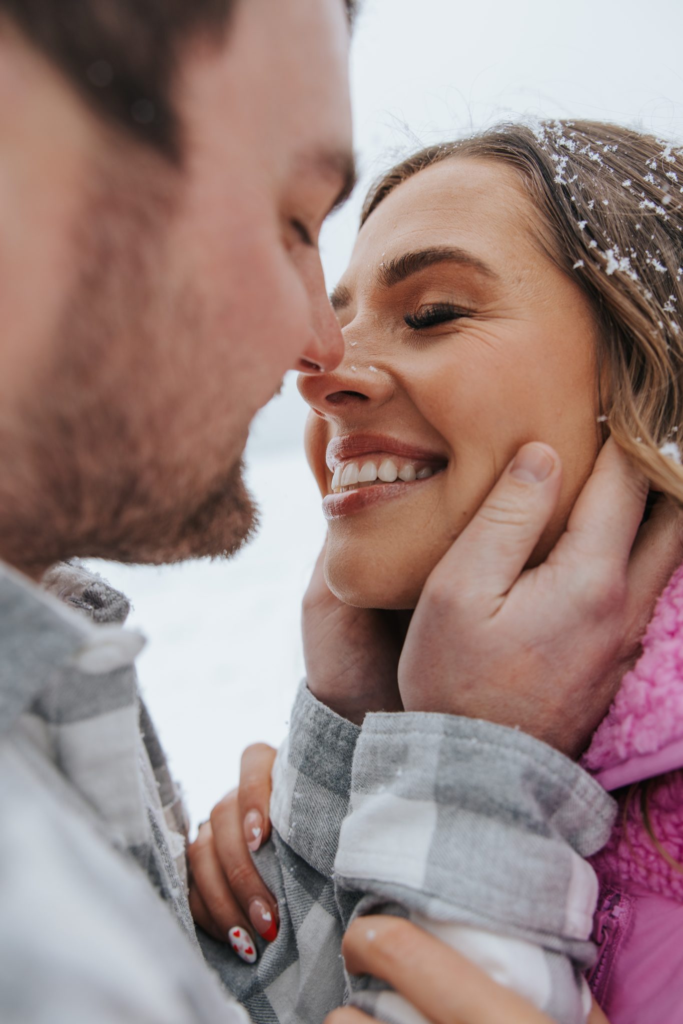 Close-up winter engagement moment – A couple shares a sweet, intimate moment in the snow, their faces nearly touching as the groom cradles the bride’s face, capturing the romance of snowy montana engagements rocky mountain bride.