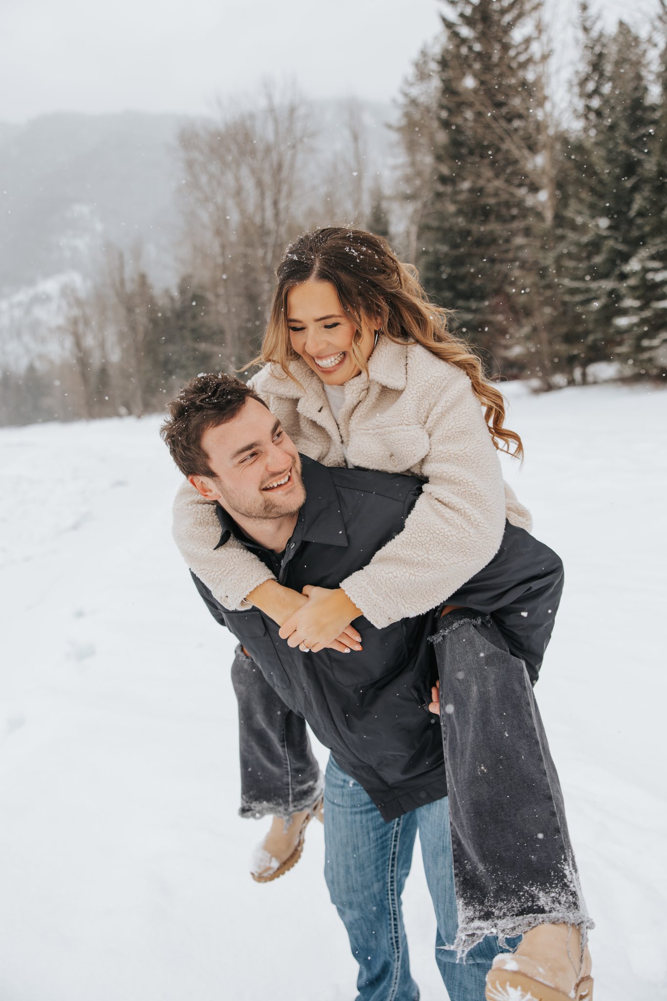 Playful piggyback ride in the snow – A bride-to-be laughs joyfully as she gets a piggyback ride from her fiancé in a snow-covered Montana landscape, perfectly showcasing snowy montana engagements rocky mountain bride.