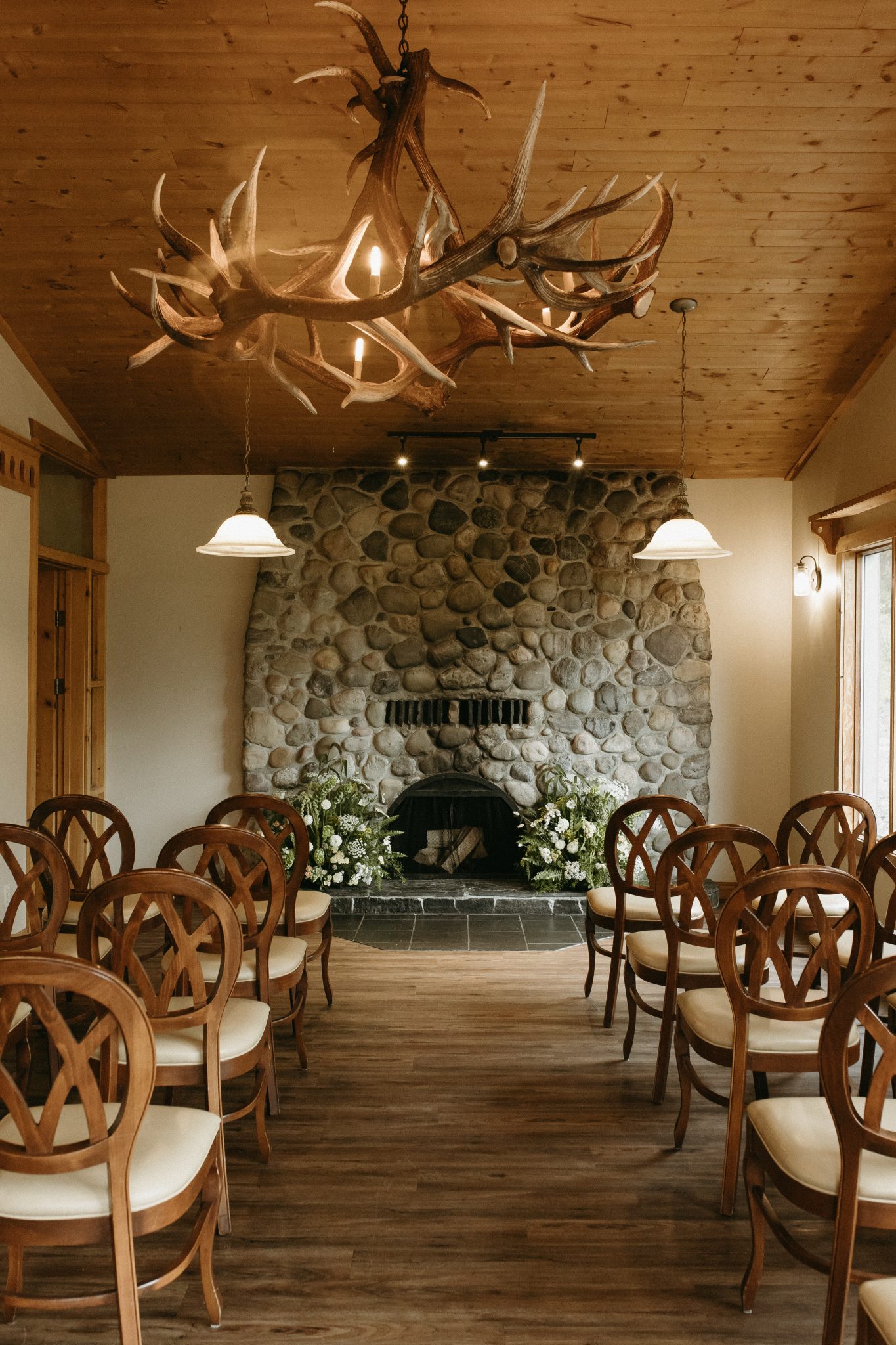 A cozy indoor ceremony space with a stone fireplace, adorned with white floral arrangements, creating a warm and intimate Alberta summer wedding setting.