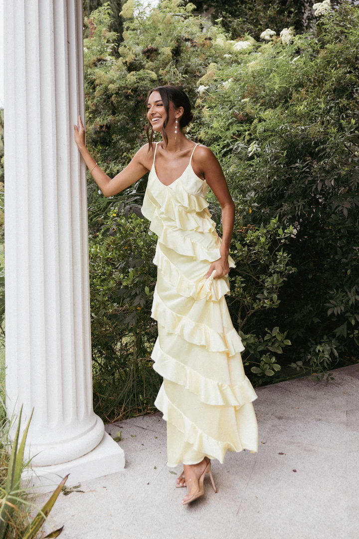 A dreamy pale yellow satin maxi dress with delicate ruffles, designed for a romantic wedding celebration.