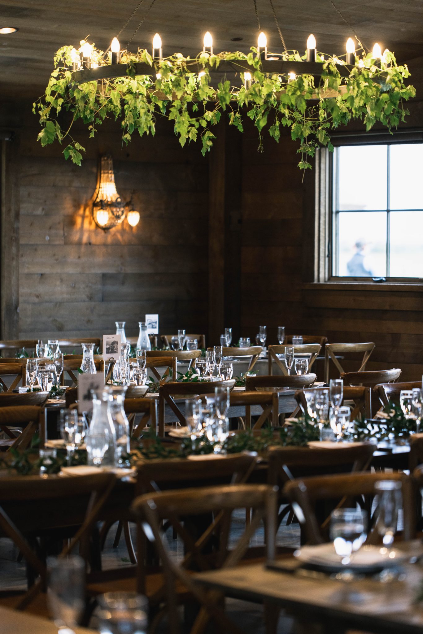 A warm and inviting reception space at a Copper Rose Ranch Montana wedding rocky mountain bride, with rustic wooden tables, candlelit glassware, and greenery-adorned chandeliers enhancing the cozy ambiance.