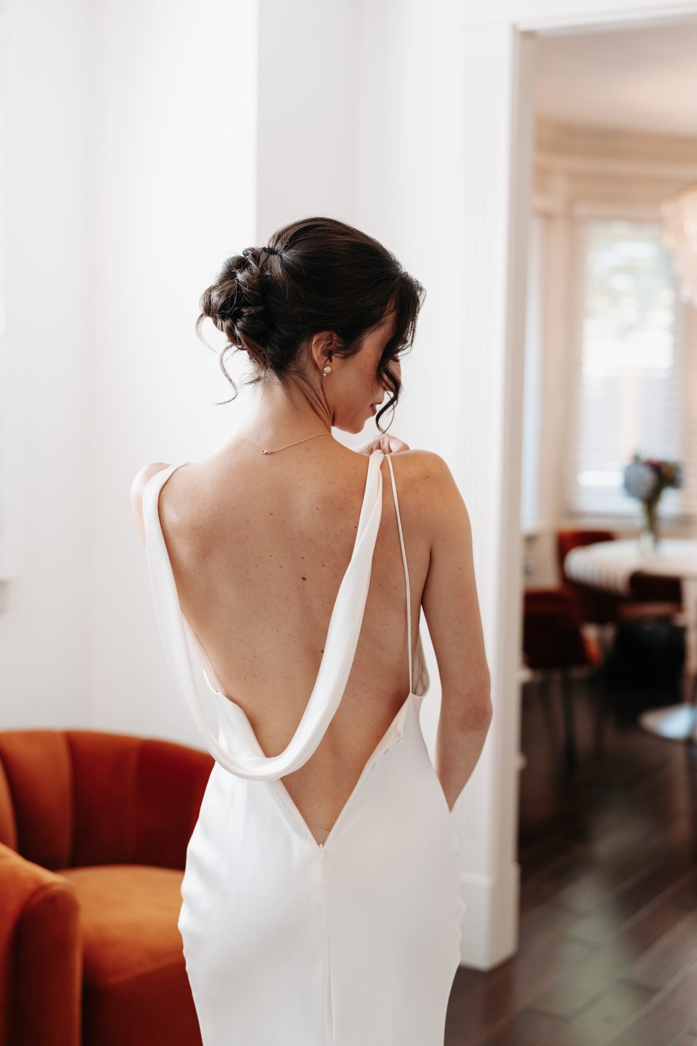 Bride in a stunning backless gown adjusting her dress straps, captured in a bright and elegant room during a Denver Botanic Gardens wedding.