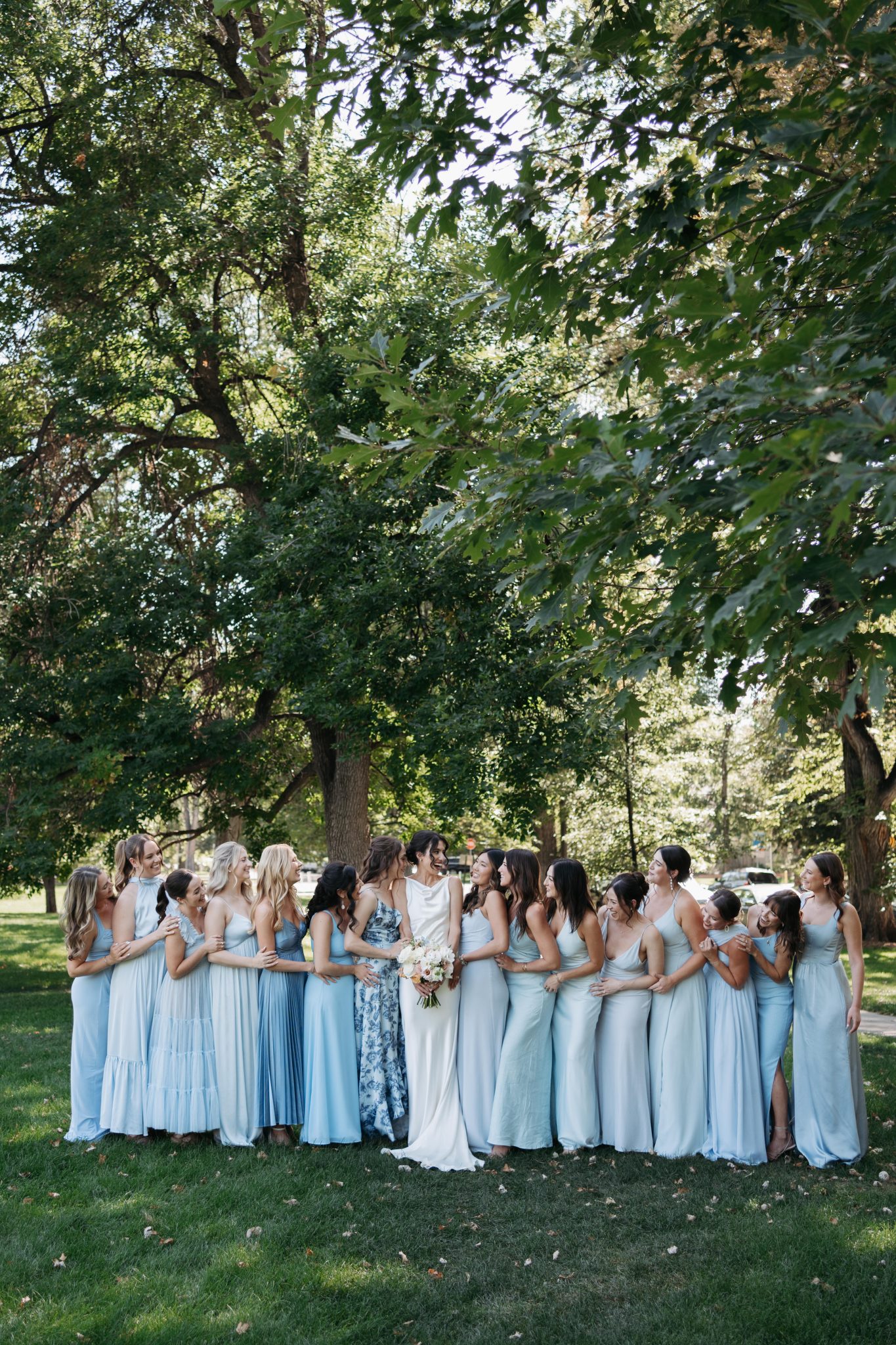 Bride surrounded by her bridesmaids in light blue dresses, laughing together outdoors at a Denver Botanic Gardens wedding.