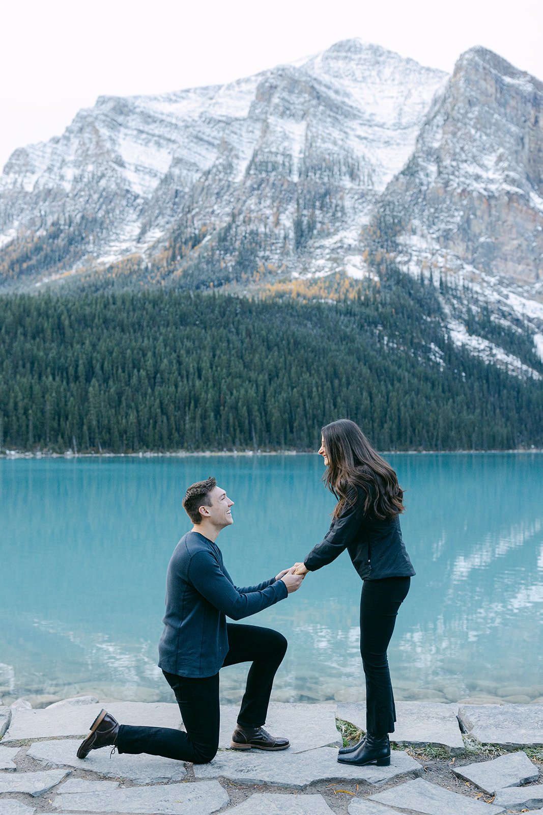 Lake Louise Banff National Park Surprise Proposal – A romantic moment as a man kneels on one knee by the turquoise waters of Lake Louise, proposing to his partner with the stunning snow-capped mountains in the background.