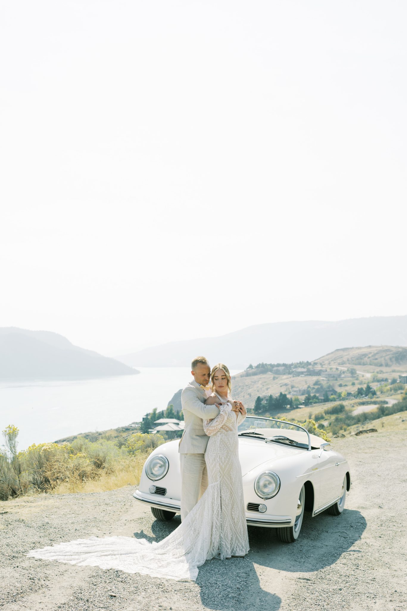 Bride and groom embracing near a vintage convertible with a stunning mountain view at a Sunshine CC Bloom Flower Farm summer wedding.