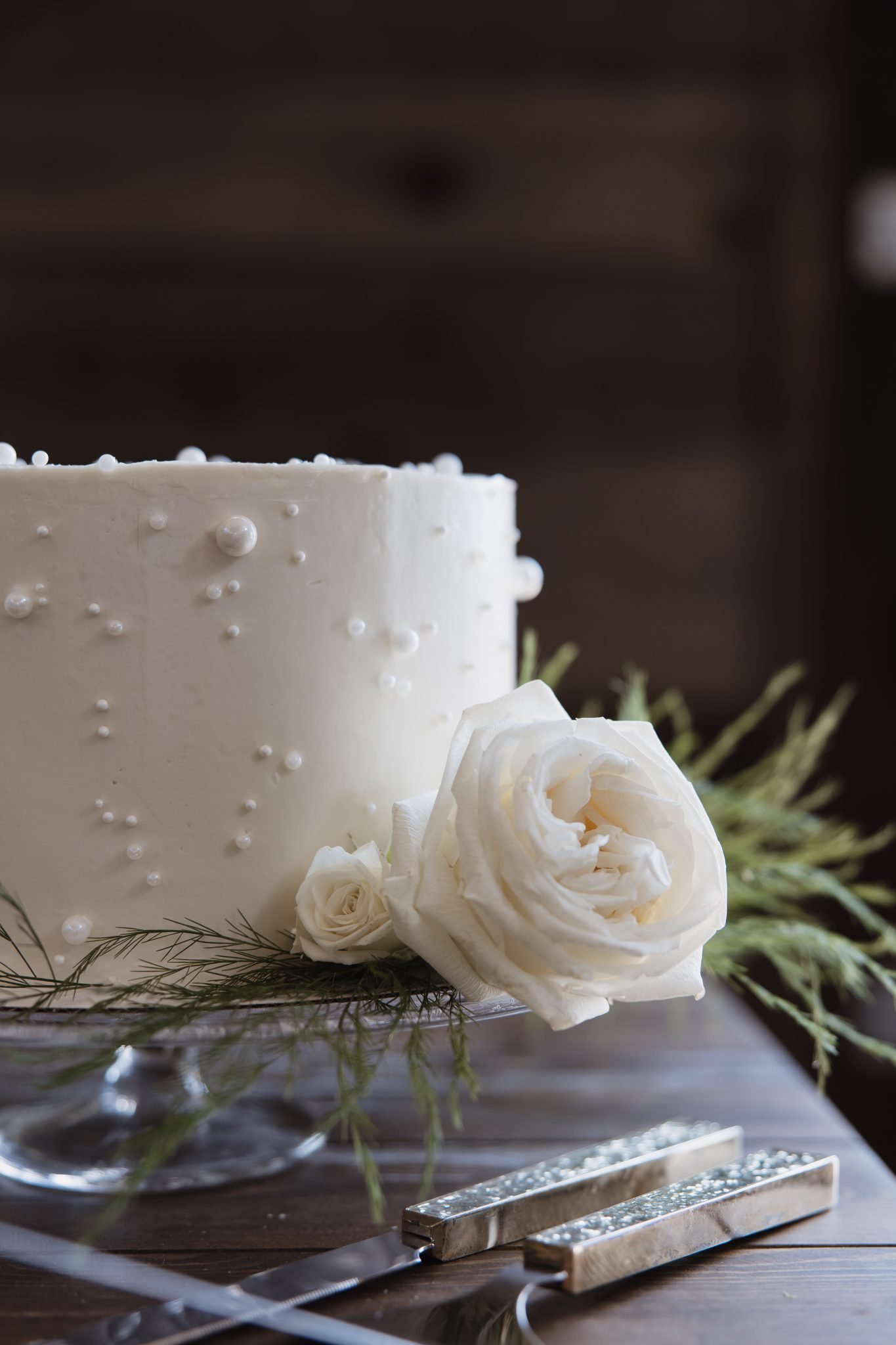 A minimalist white wedding cake adorned with pearl details and fresh white roses, perfectly styled for The Meadows on Rock Creek White Wedding.