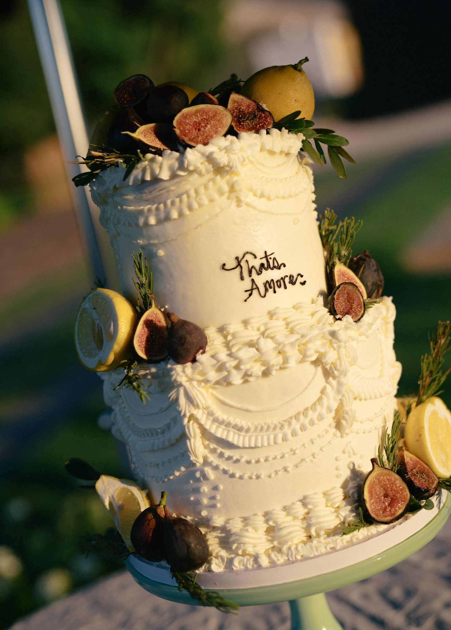 Two-tiered white cake decorated with figs, lemons, and fresh greenery as part of a White Barn wedding inspiration.