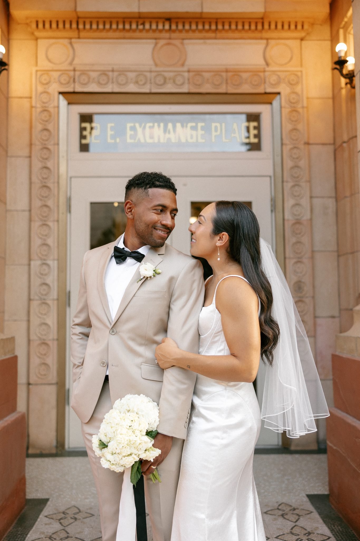 A newlywed couple standing outside the historic commercial club salt lake city utah, smiling at each other in timeless wedding attire.