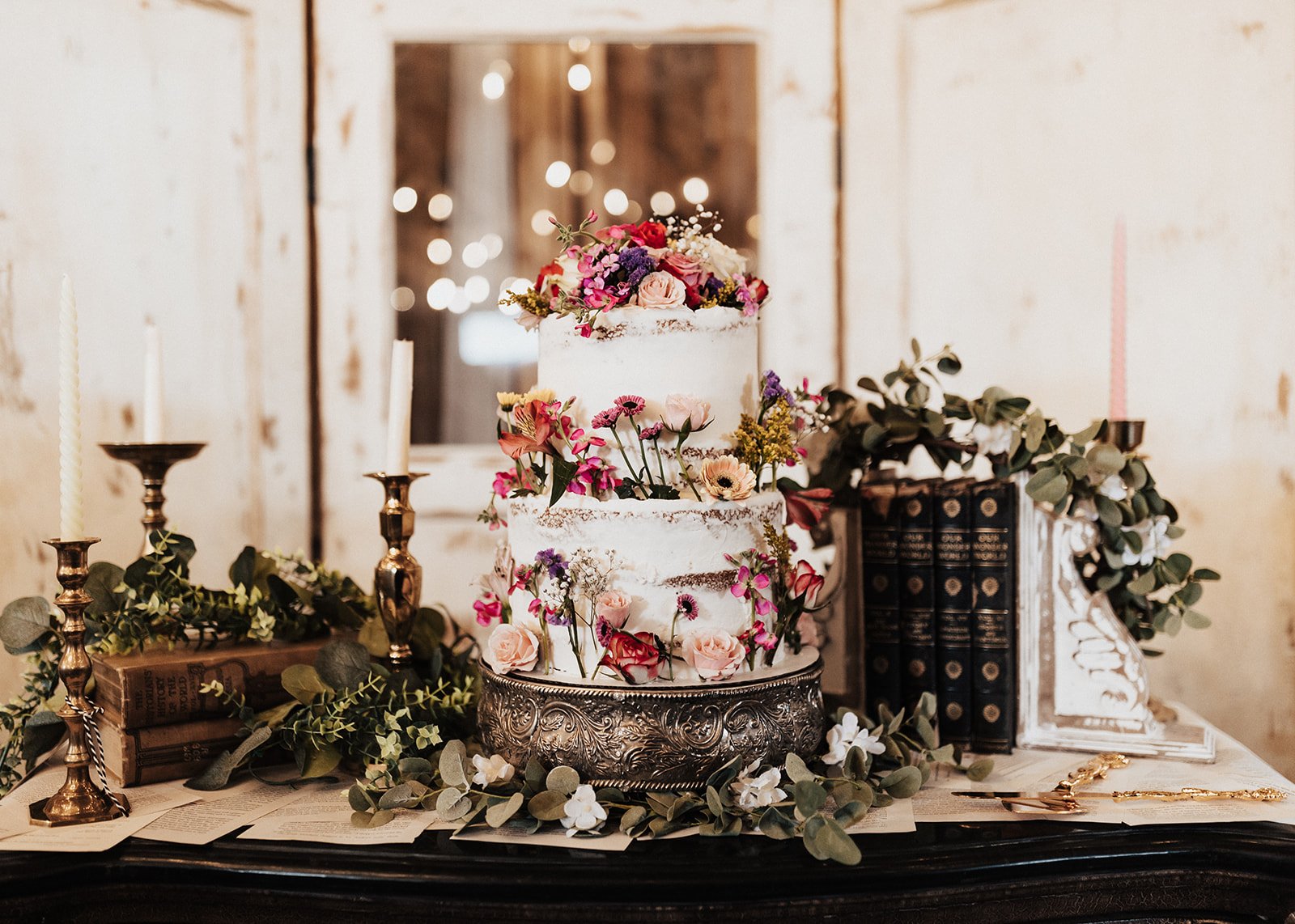 Three-tiered wedding cake adorned with fresh flowers and antique brass accents at a fall Utah wedding reception.