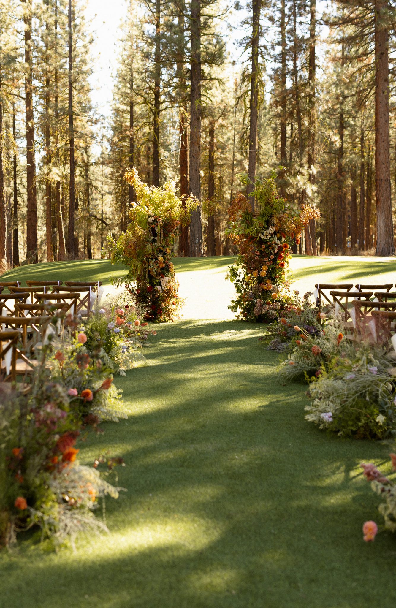A dreamy outdoor ceremony setup with lush floral arrangements lining the aisle, surrounded by towering pine trees, creating a picturesque backdrop for a Lake Tahoe Winter Wedding.