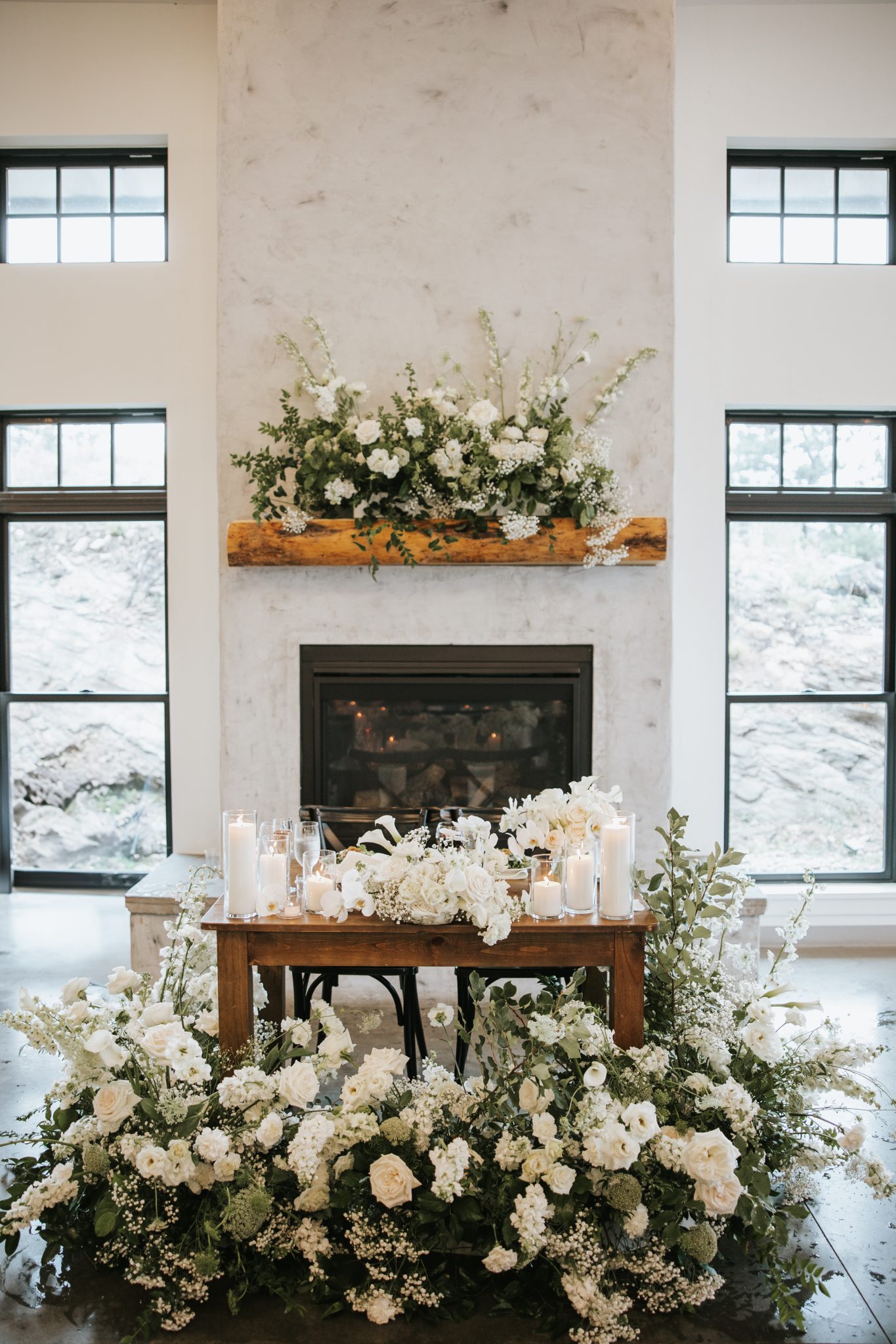 A cozy and elegant sweetheart table styled with white florals and candlelight against a fireplace backdrop, highlighting the charm of a North Start Gathering wedding in Idaho Springs Rocky Mountain Bride.