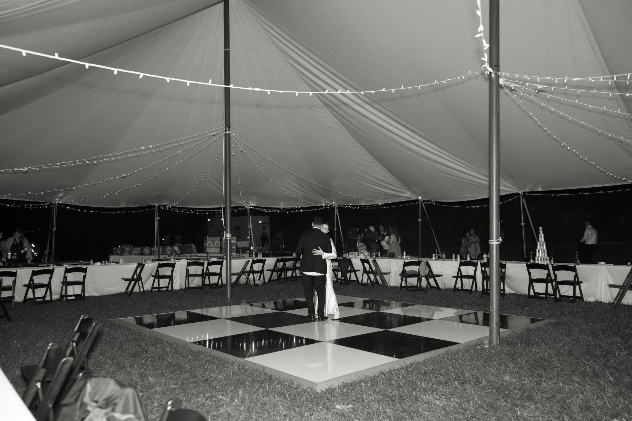 Bride and groom share their first dance on a checkered floor under string lights at a Private Property Tented Wedding in New Mexico.