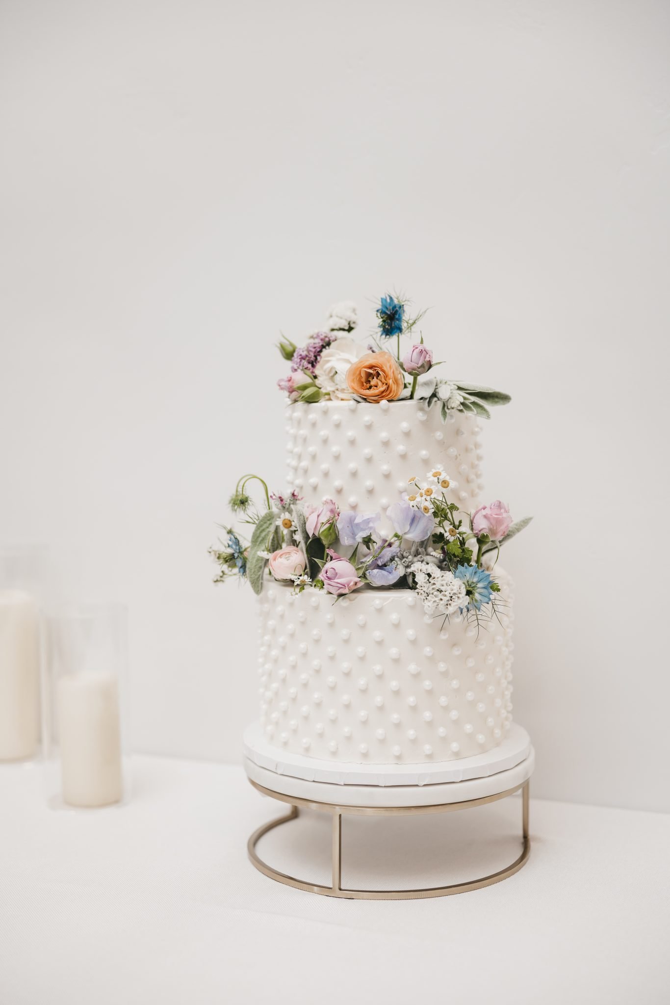 Two-tier white wedding cake with dotted texture and vibrant fresh florals in spring colors, photographed by VILVD Photography Nevada Wedding Photographer.