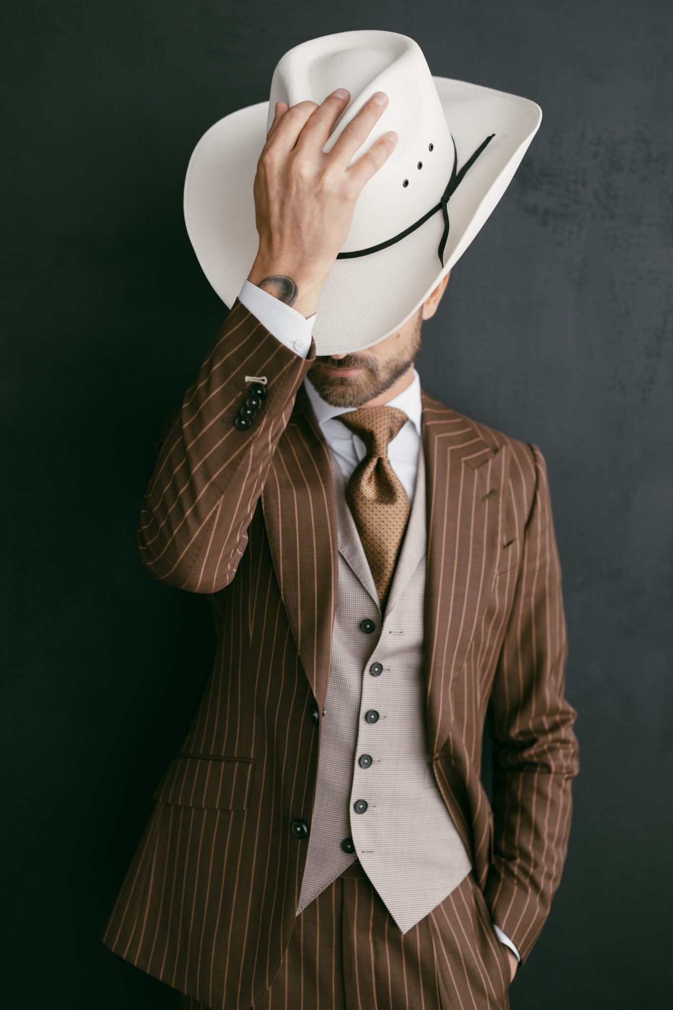 Groom in a brown striped suit and beige vest holding a white cowboy hat for The Gallery Studio wedding inspiration rocky mountain bride.