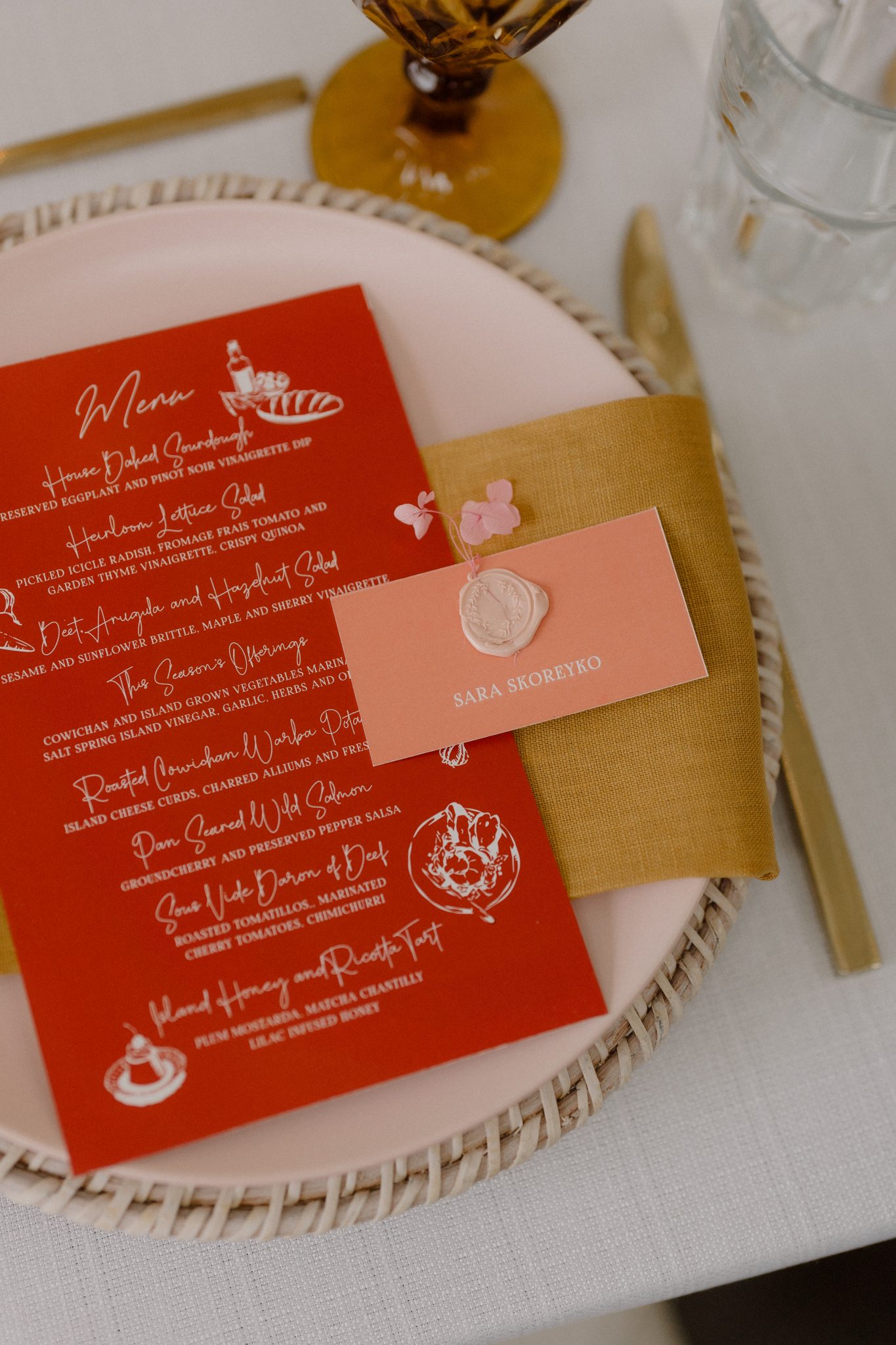 A vibrant reception place setting with a bold red menu, mustard linen napkin, and personalized name card at a Vancouver Island fall wedding rocky mountain bride.