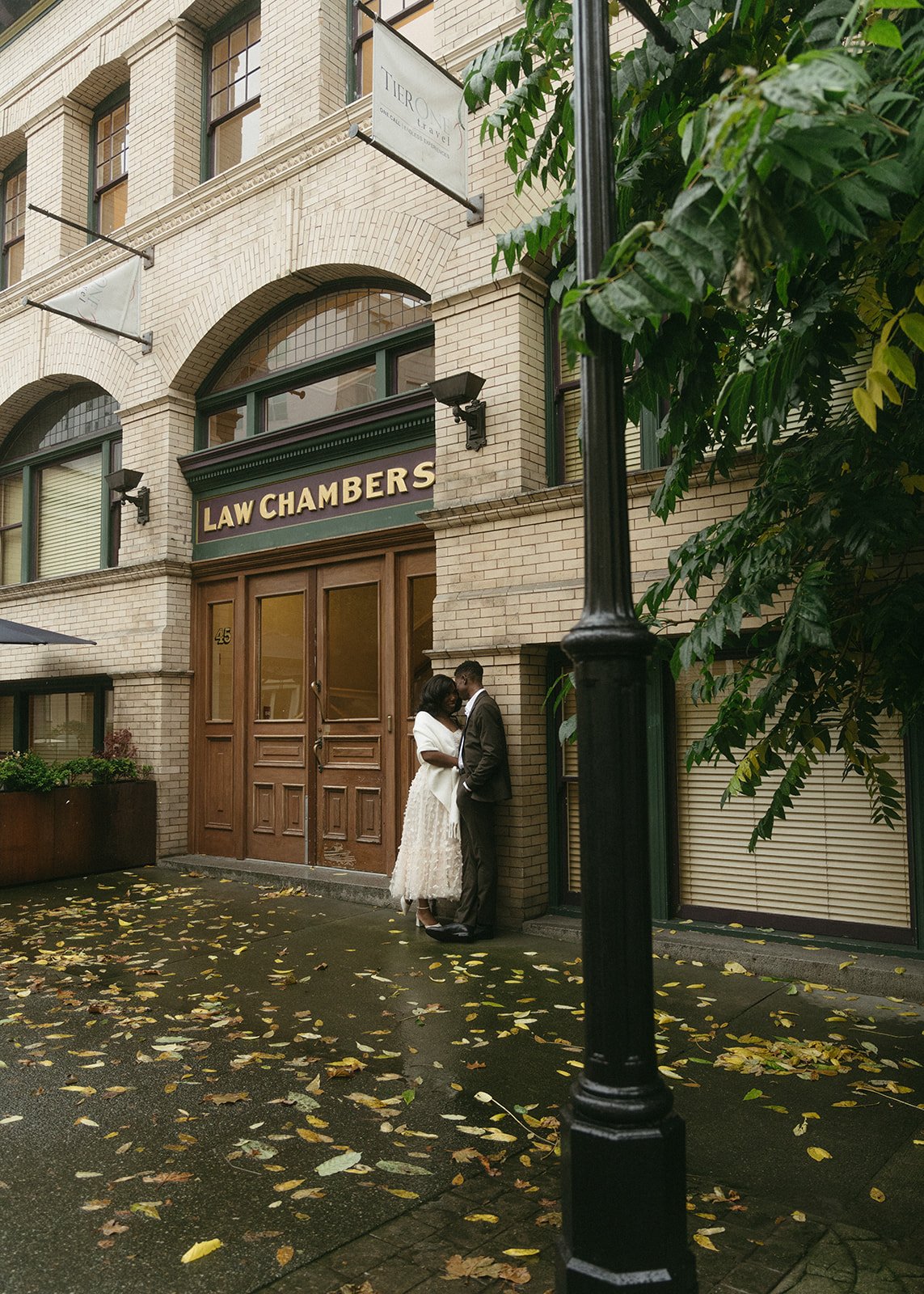 Couple embraces in front of the historic law chambers near kinu uptown victoria vancouver island, surrounded by autumn leaves and urban charm.